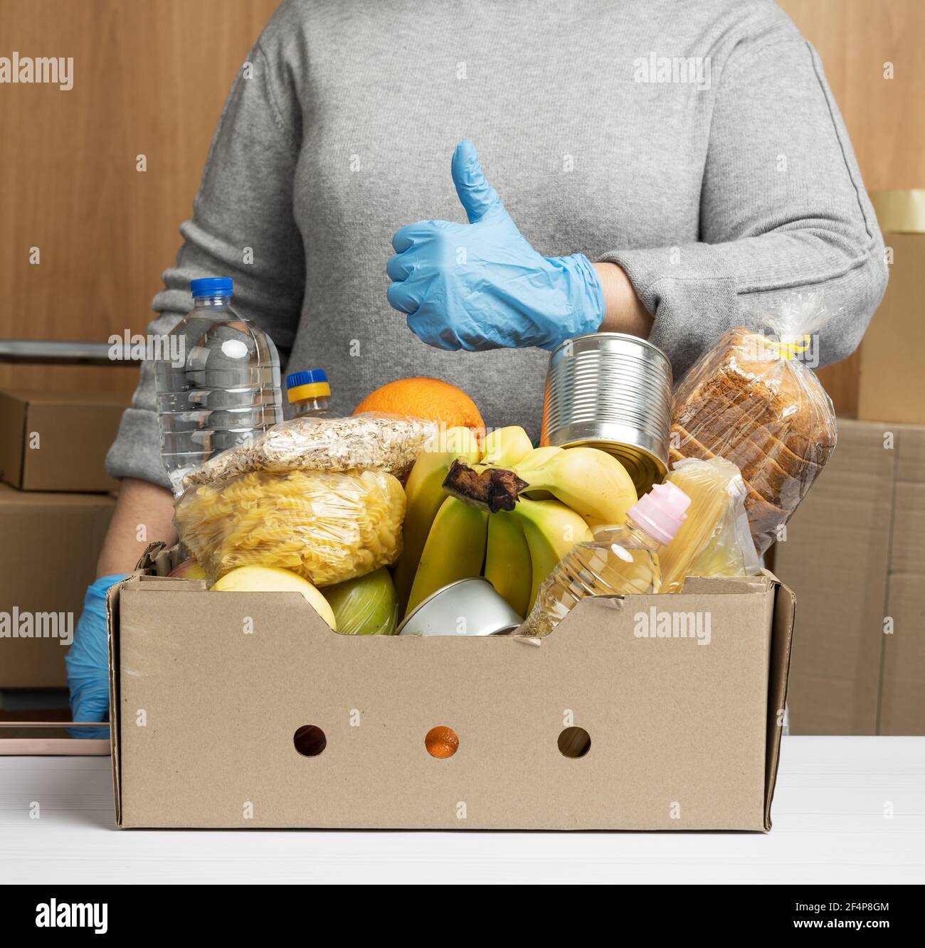 Frau in Handschuhen sammelt immer wieder Lebensmittel, Früchte und Dinge und einen Karton für die Hilfe für Bedürftige, das Konzept der Hilfe und Freiwilligenarbeit. Lieferung Stockfoto