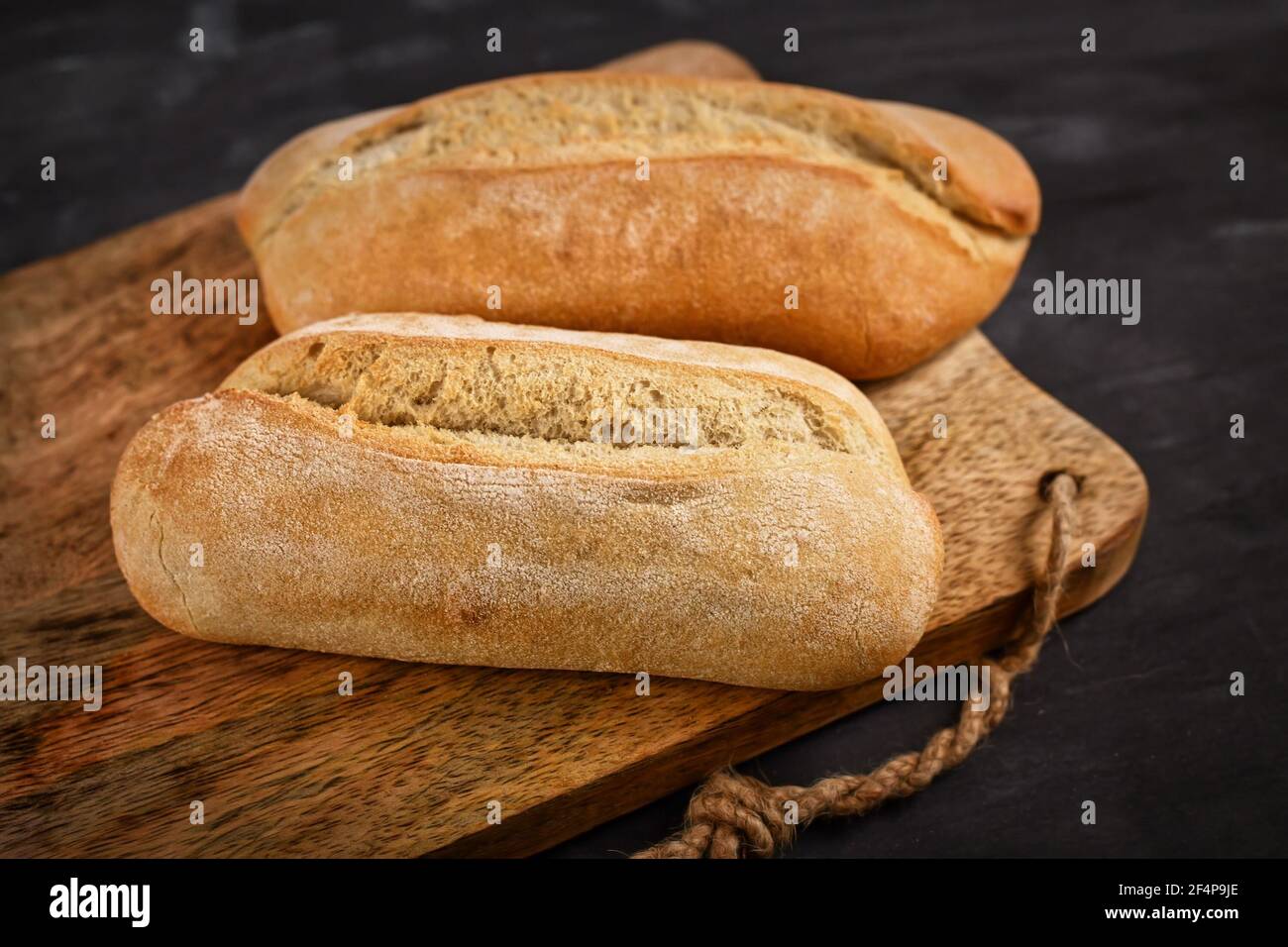 Rustikale Brötchen auf Holzschneidebrett auf dunklem Tisch Stockfoto
