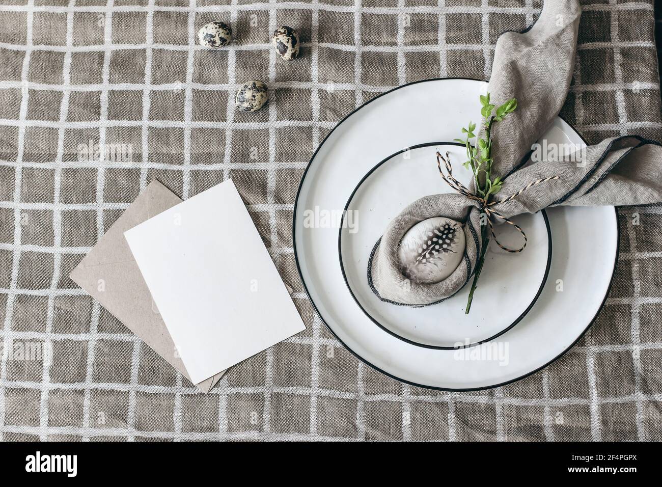 Ostern dekorative Tischdekoration. Frühlingsstill-Leben mit Grußkarte Mockup, Wachtel und Hühnereier. Teller, Serviettenfaltdeko auf beigefarbenem Leinenreiter Stockfoto
