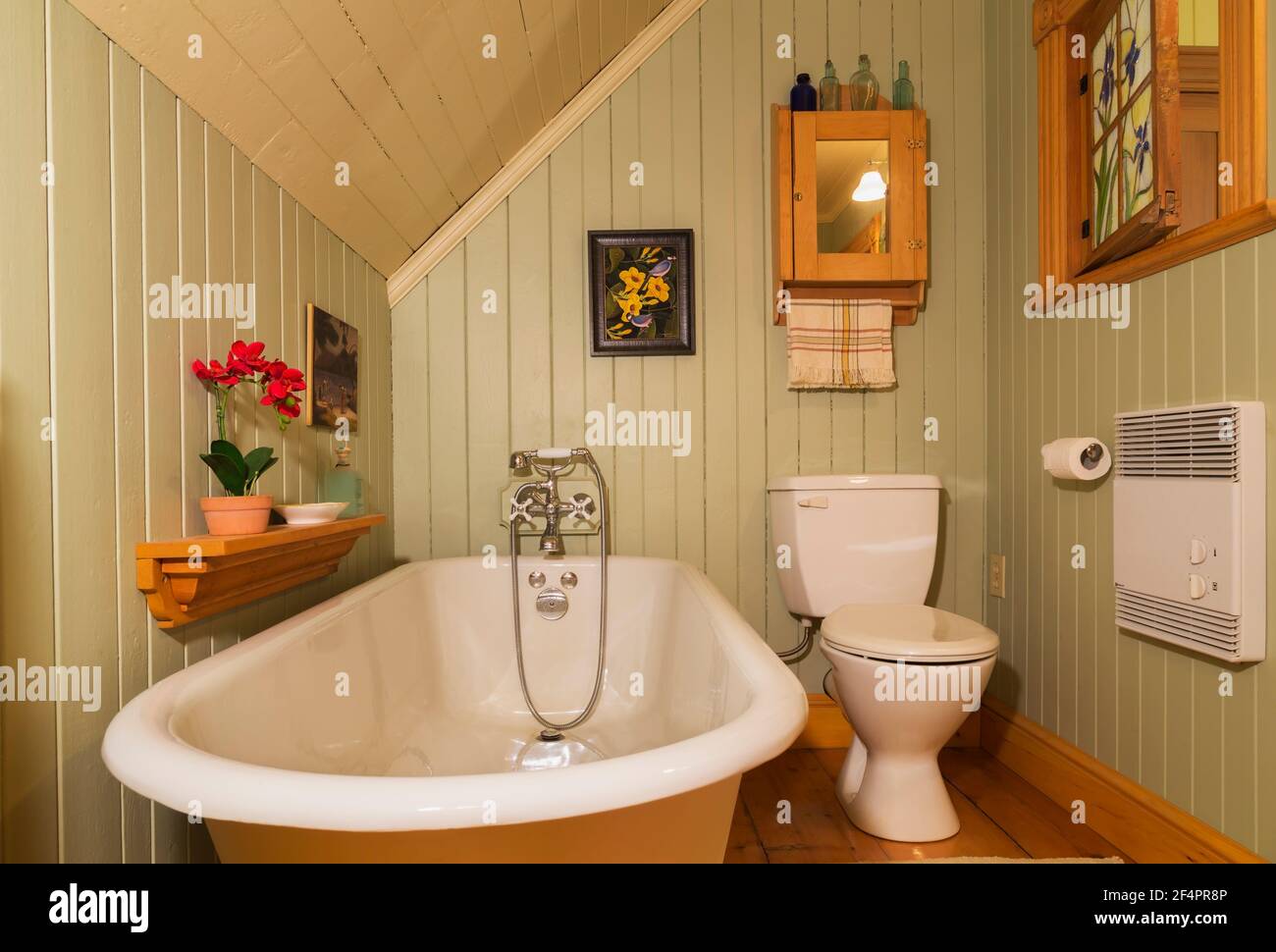 Freistehende rollstuhlgerechte Badewanne mit Füßen in grün und beige lackiertem Holz, Badezimmer mit östlichen Hemlockböden, geöffnetem Buntglasfenster Stockfoto