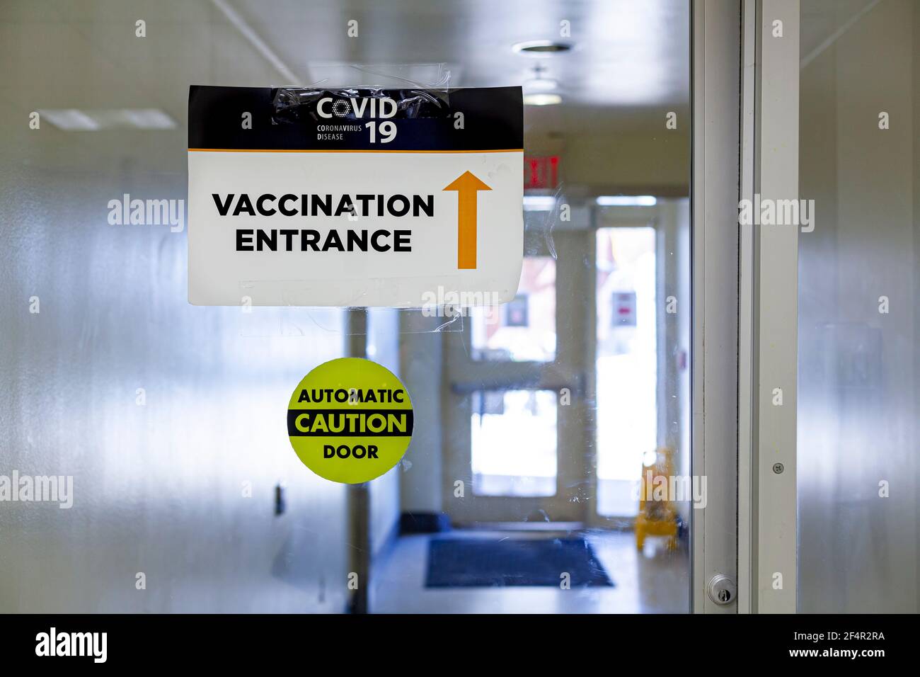 Bild zeigt das Innere einer Gesundheitseinrichtung mit Glas Automatische Tür mit einem Schild auf der Aufschrift Eingang von Die Impfstelle COVID-19 Stockfoto