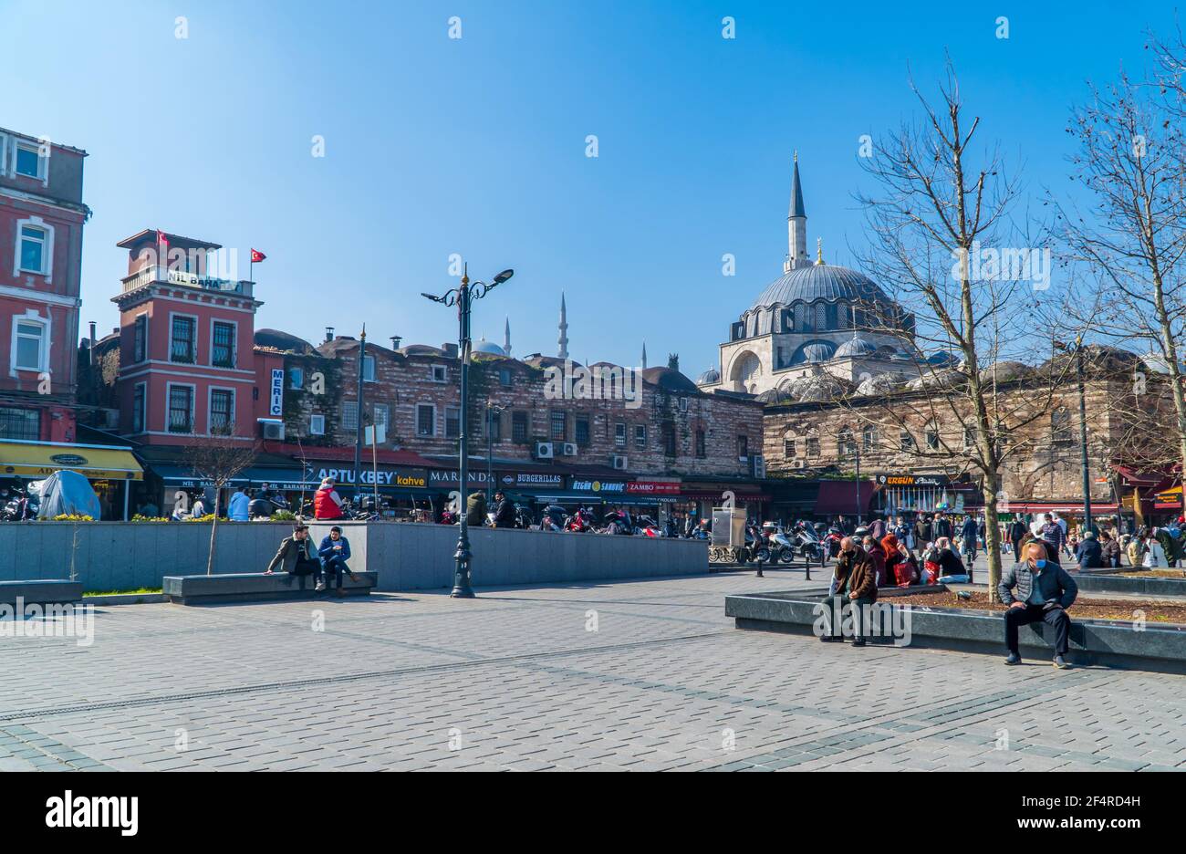 Istanbul, Türkei - 23. Februar 2021 - Straßenfotografie von Menschen auf dem Eminönü-Platz mit der Rüstem-Pasa-Moschee an einem sonnigen Tag Stockfoto