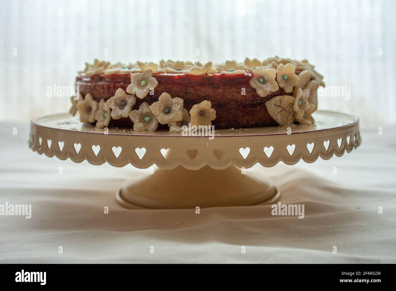 Dunkler Kuchen mit hellen Marzipan-Blumenschmuck und Zuckerperlen für Blütenknospen, auf einem Kuchenständer. Stockfoto