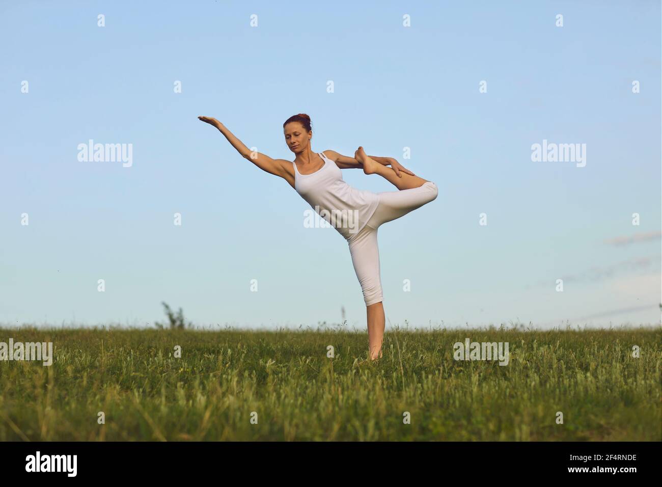 Slim Yoga-Lehrer tun stehende Bogen Pose auf grünen Sommer Wiese unter klarem blauen Himmel Stockfoto