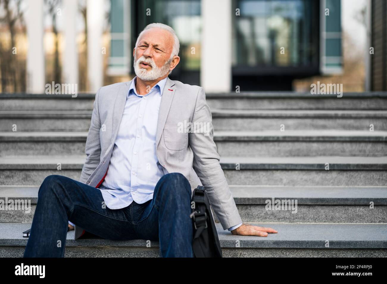 Ein leitender Geschäftsmann ist der Arbeit müde. Er sitzt auf einer Treppe vor dem Firmengebäude. Stockfoto