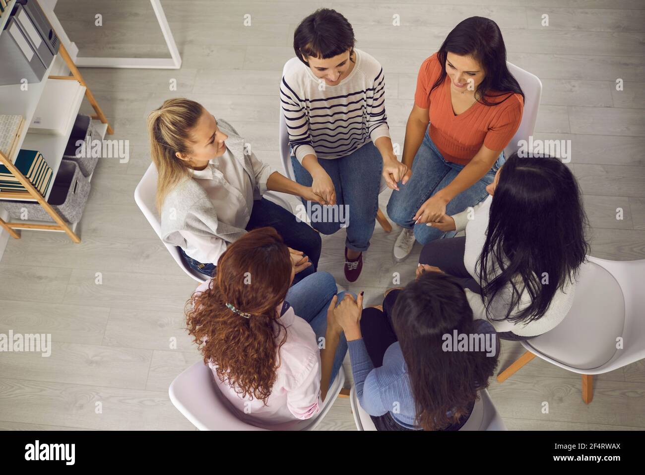 Glückliche Frauen sitzen im Kreis und halten die Hände in der Sitzung Mit Trainer oder in der Gruppentherapie Stockfoto