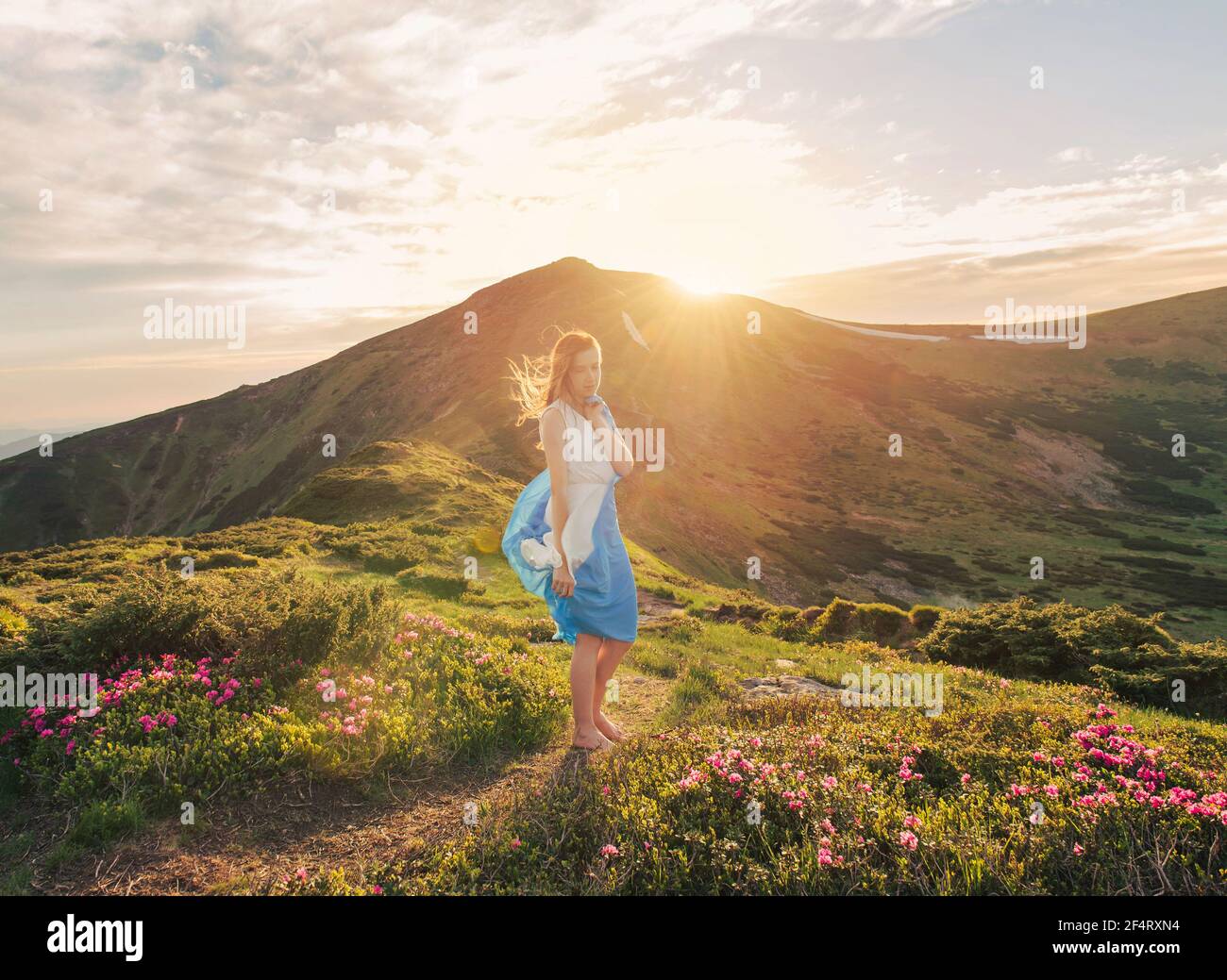 Frau fühlt Freiheit und genießt die Natur in den Bergen Mit blauem Gewebe in den Händen bei Sonnenuntergang Stockfoto