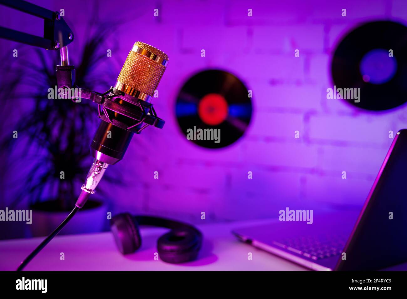 Aufnahme Podcast - Mikrofon-Kopfhörer und Laptop im Heimstudio. Neonlichter Stockfoto