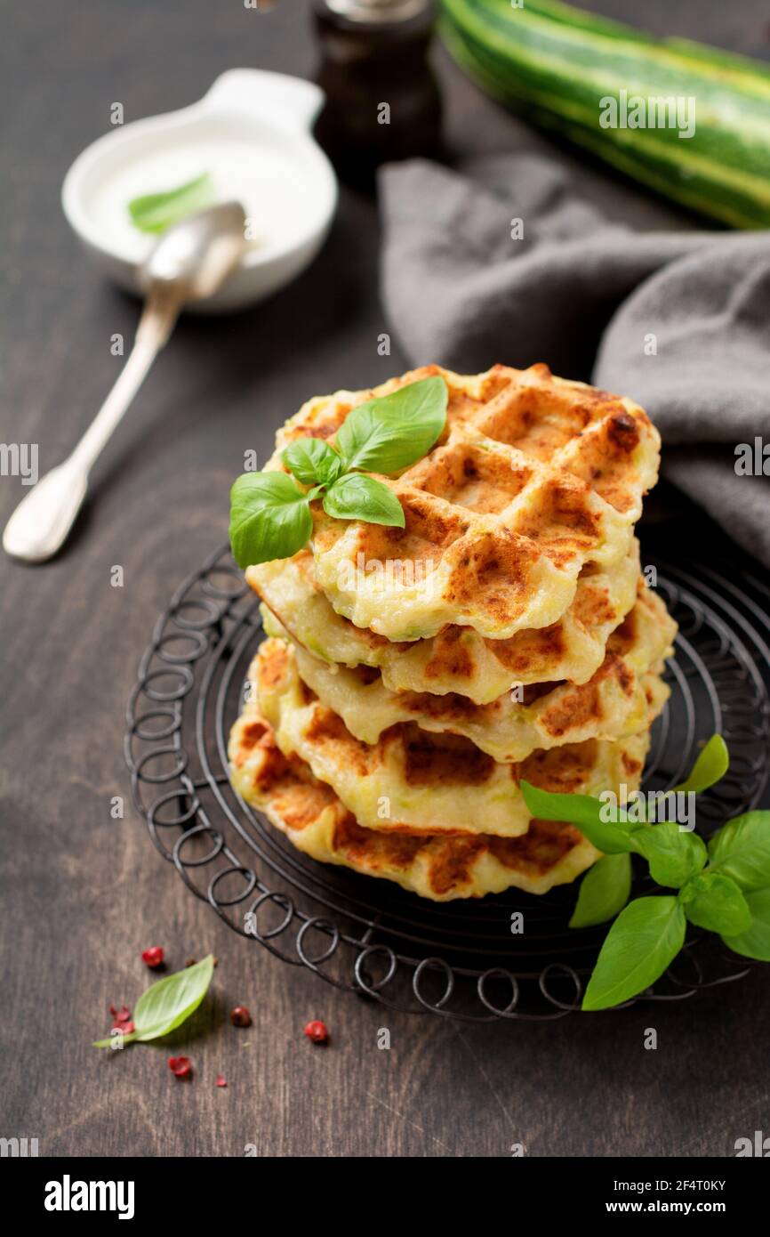 Hausgemachte Zucchini Waffeln Stapel mit Käse, Sause und Blatt Basilikum auf alten Holz dunklen Hintergrund. Konzept der Keto Ernährung Lebensmittel. Selektiver Fokus Stockfoto