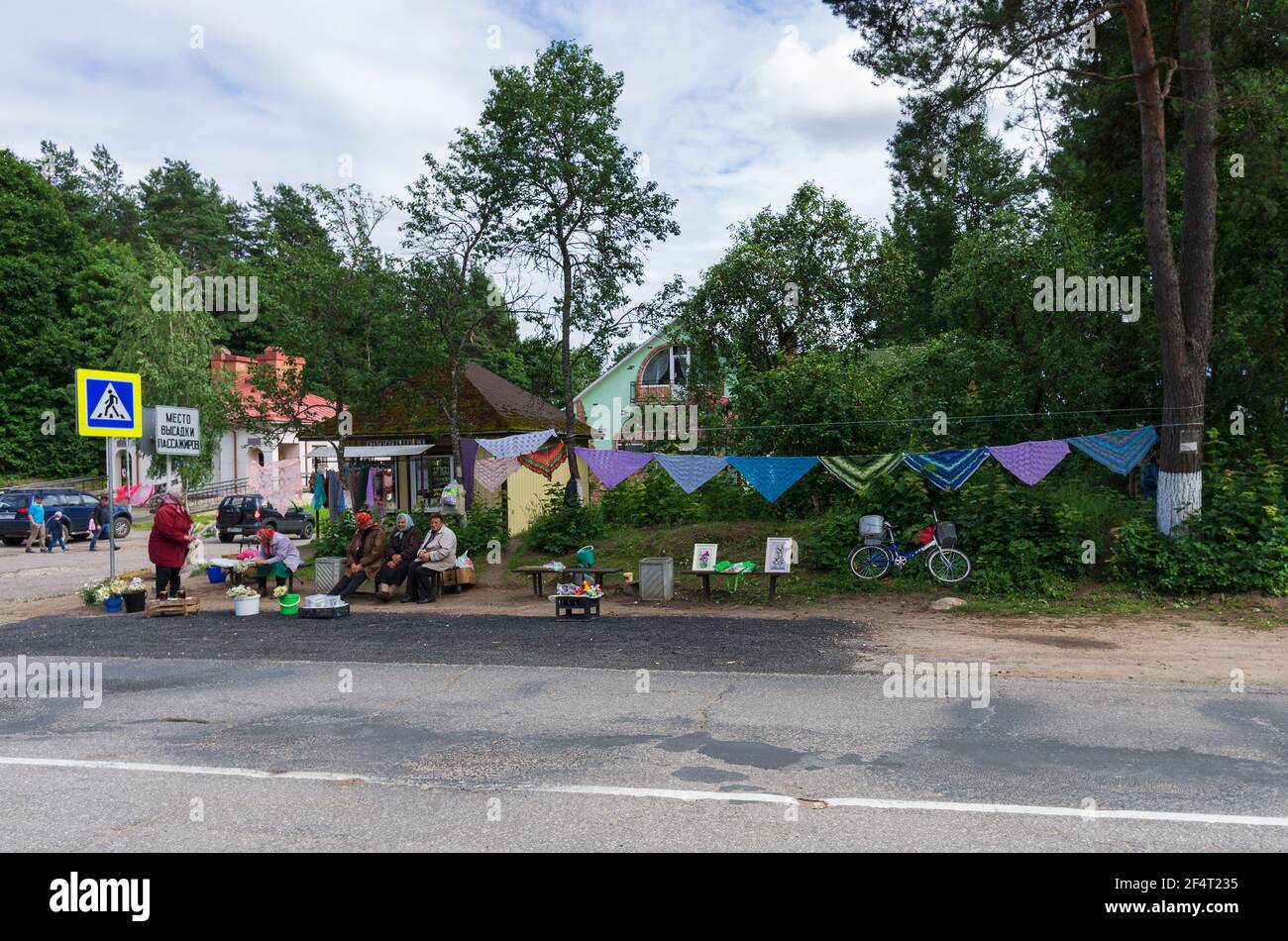 Pushkinskiye Gory, Pskov Oblast, Russland - 07. Juli 2019: Ältere pensionierte Frauen verkaufen Blumen und Tücher an einer Bushaltestelle mit Straßenschildern 'Abziehbereich Stockfoto