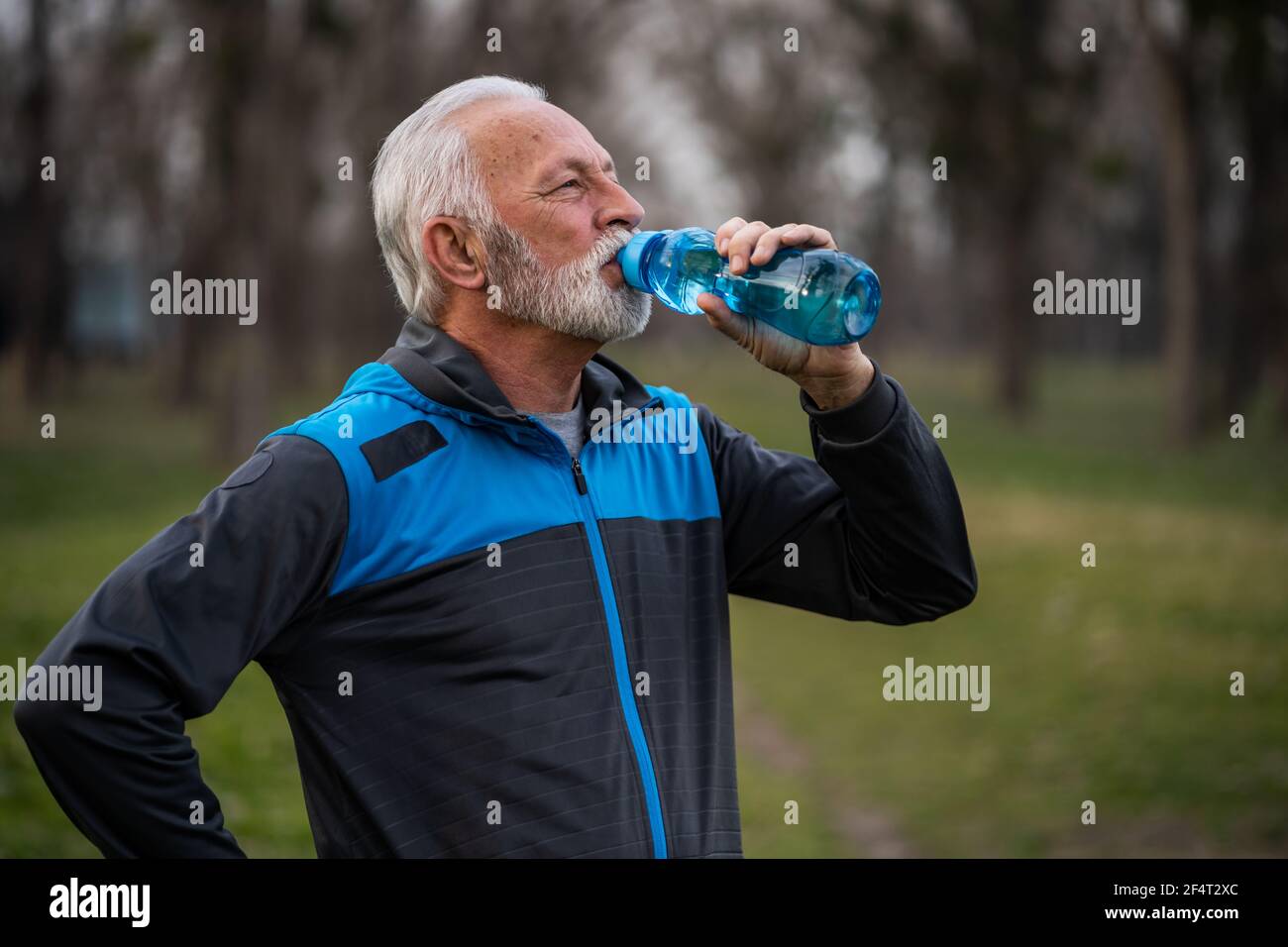 Der ältere Mann trinkt Wasser, nachdem er im Park trainiert hat. Stockfoto