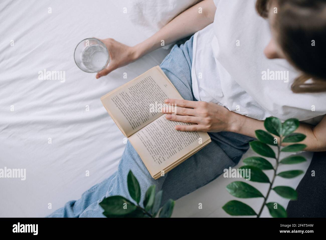 Eine junge Frau in legerer Kleidung verbringt Zeit mit dem Lesen eines Buchen Sie und halten Sie ein Glas Wasser Draufsicht Stockfoto