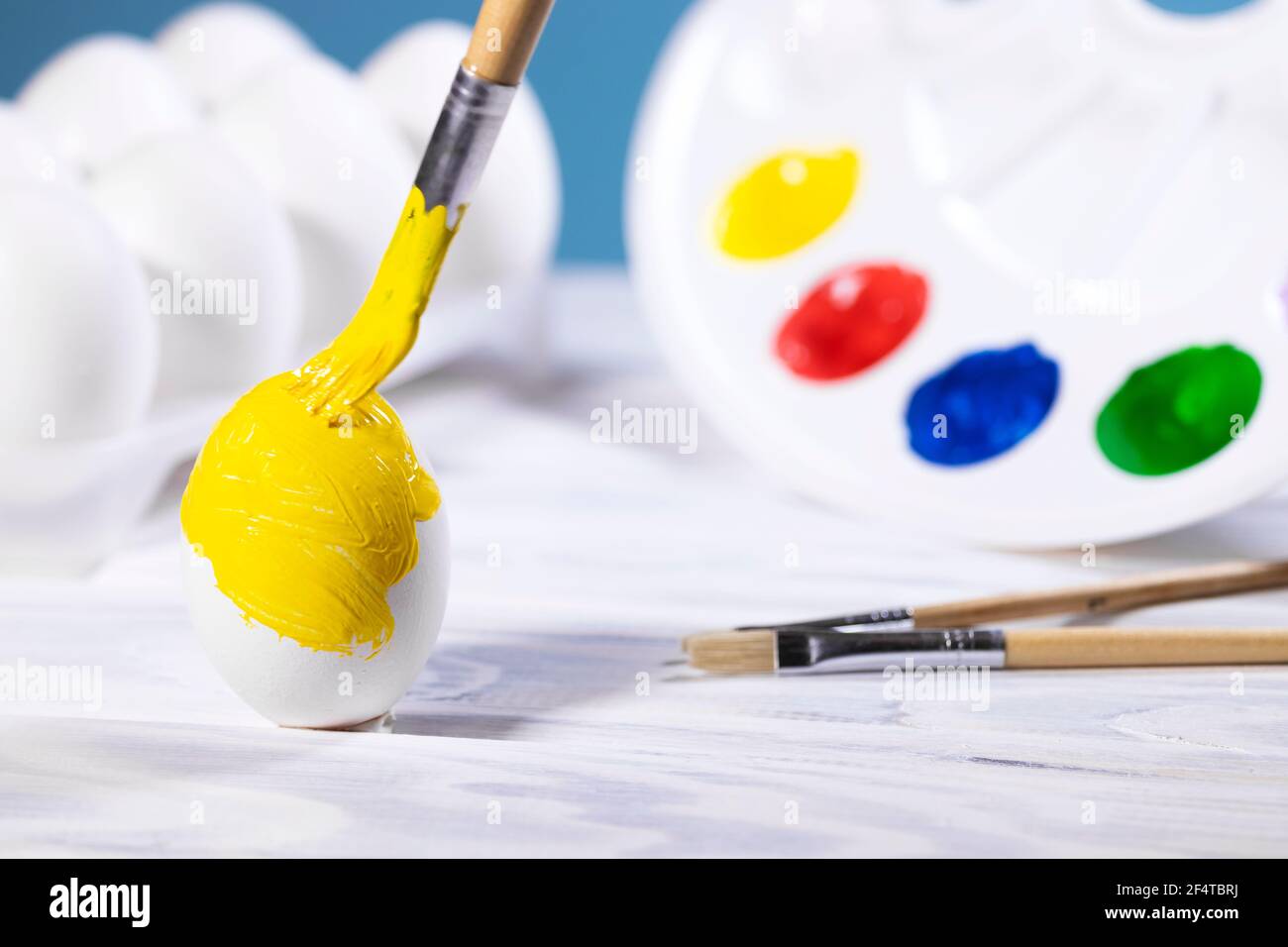 Ostereier malen, Vorbereitung für den Frühlingsurlaub, Gelbes Ei mit Farbpalette auf blauem Hintergrund, Pinsel malen, Copyspace Stockfoto