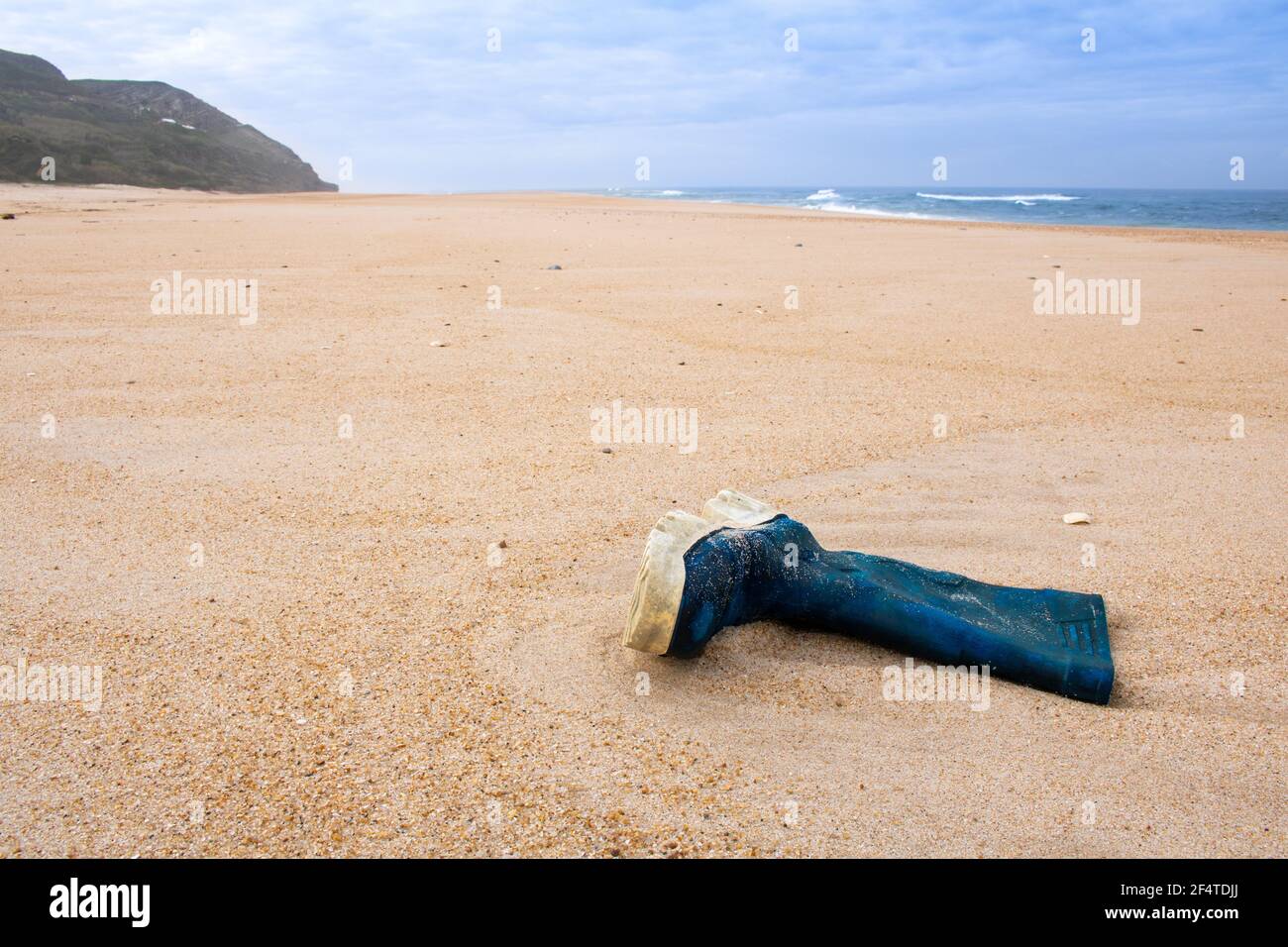 Der blaue Gummistiefel des Fischers wurde leer auf dem Sand gelassen Strand mit Meer und Berg im Hintergrund Stockfoto
