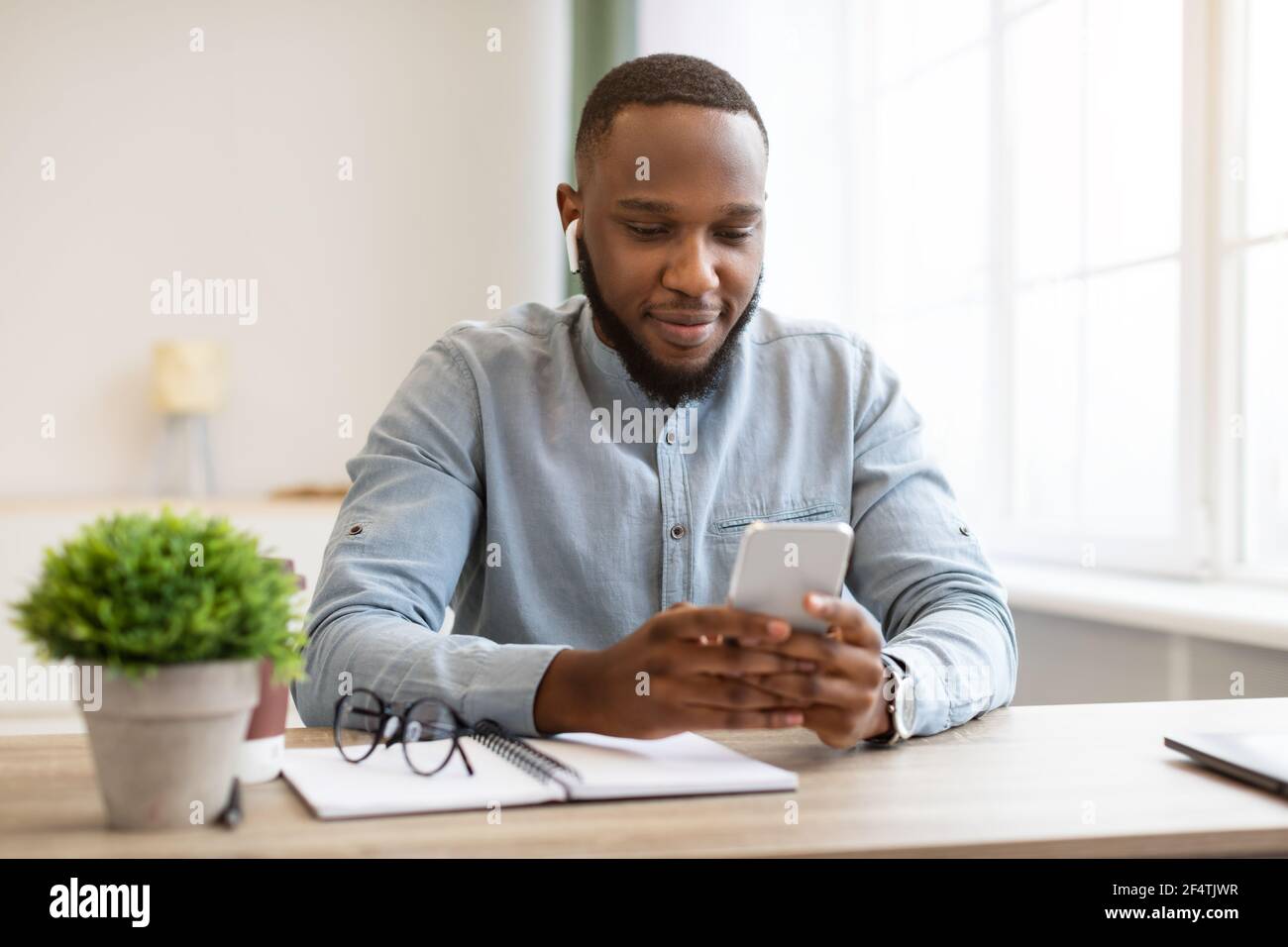 African American Business Guy Mit Smartphone Und Ohrstöpsel Im Büro Stockfoto