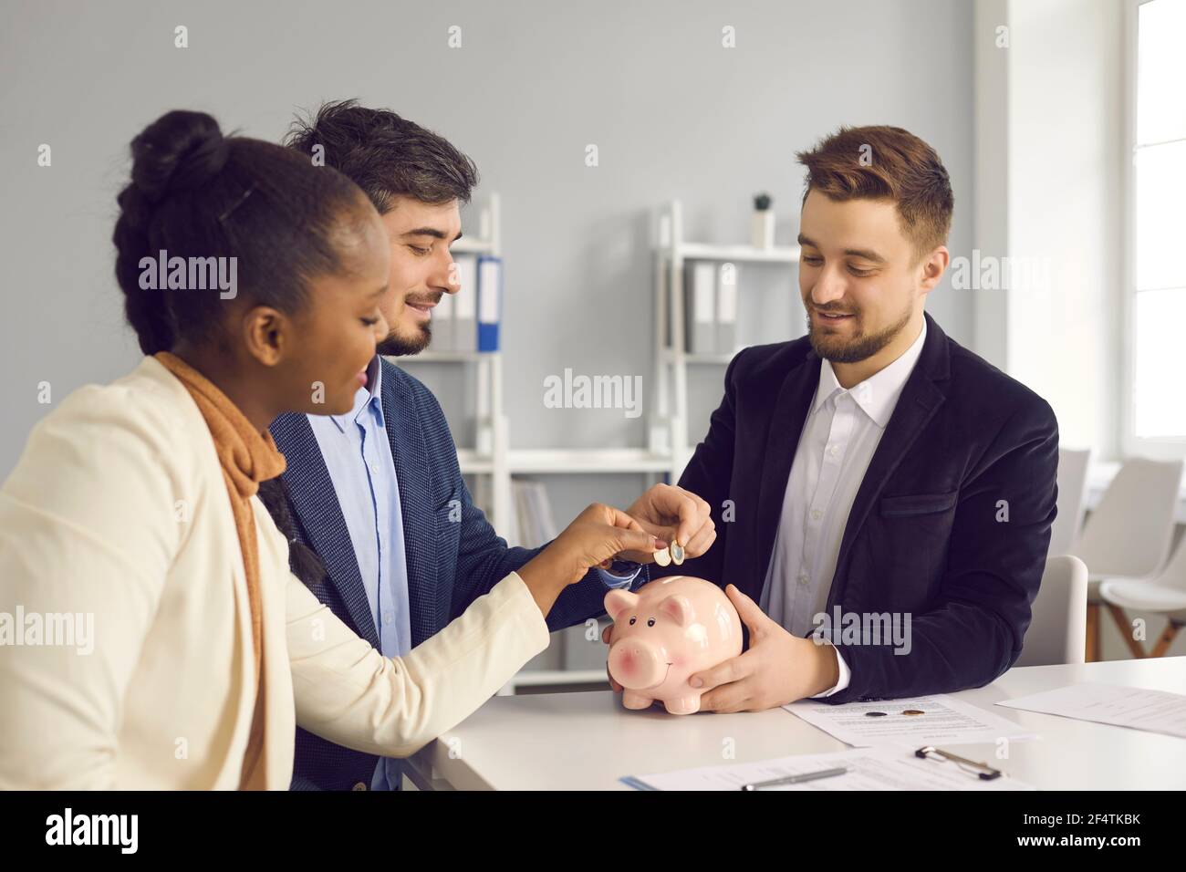 Glückliches Paar zusammen Geld in Sparschwein sitzen an Schreibtisch mit Bankberater Stockfoto