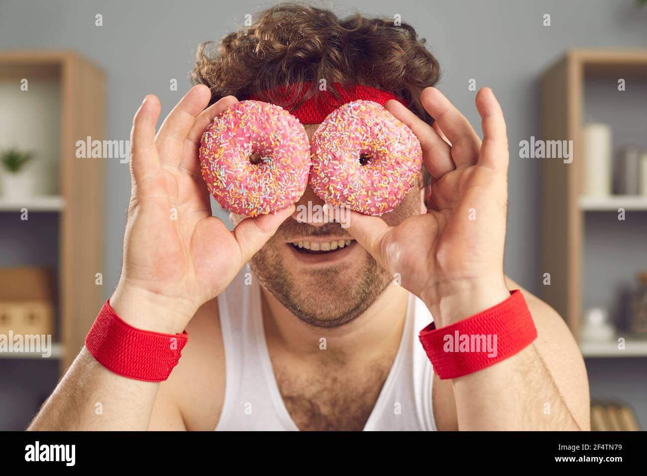 Lustig lächelnder molliger Mann bedeckt seine Augen mit einem Paar Von köstlichen rosa Donuts Stockfoto