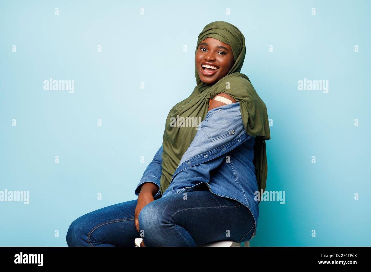 Freudig Geimpft African Muslim Lady Posiert Zeigt Arm, Blauer Hintergrund Stockfoto