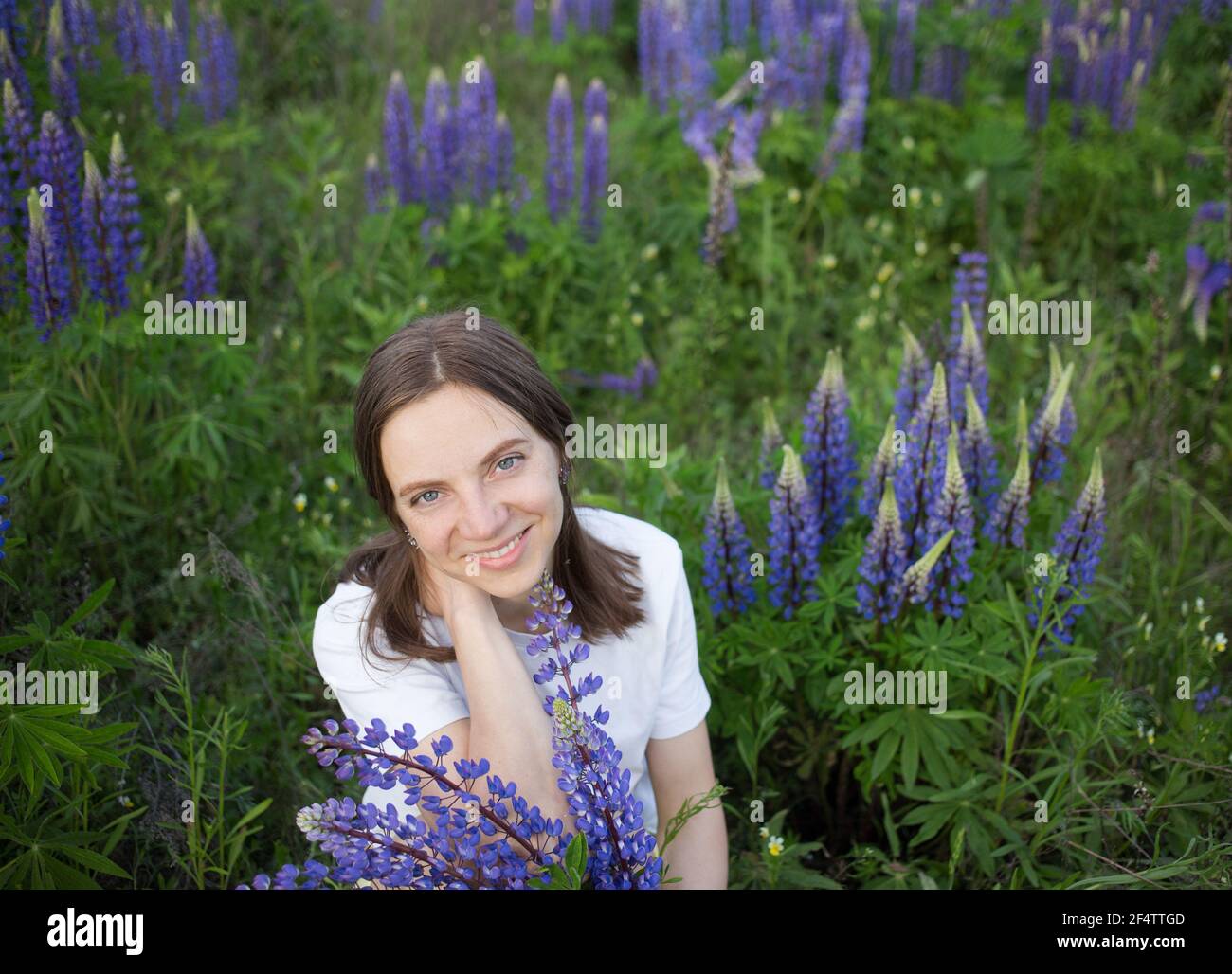 Schöne lächelnde Frau 35 Jahre alt unter blauen - lila Lupinen Wildblumen auf der Wiese. Weibliche Porträt in der Natur. Digitale Entgiftung, Sommerwochenende. E Stockfoto