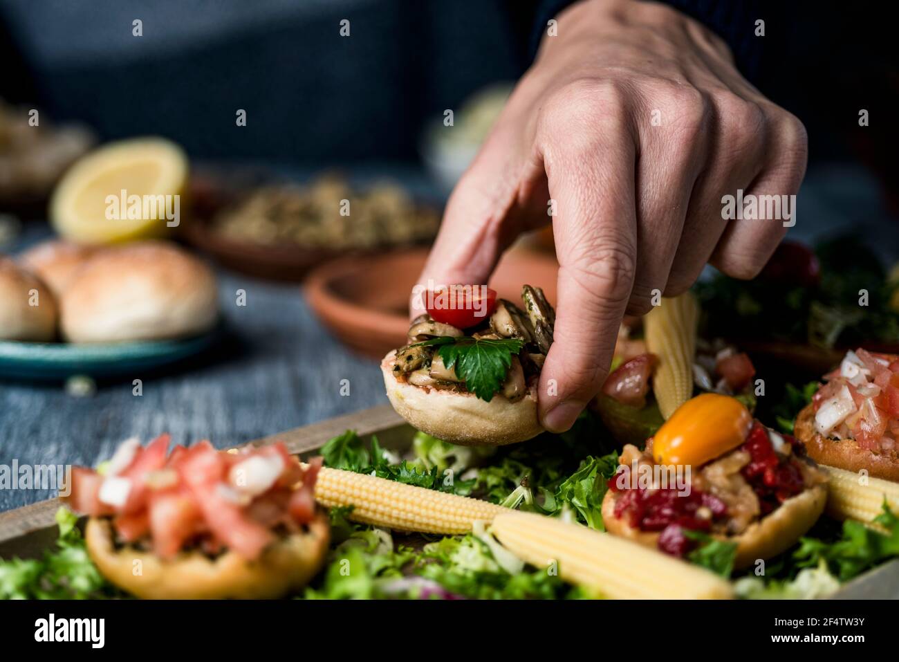 Nahaufnahme eines jungen kaukaisanischen Mannes, der eine Vorspeise aus einem Holztablett mit verschiedenen veganen Vorspeisen, mit verschiedenen Belägen, auf einem gr Stockfoto
