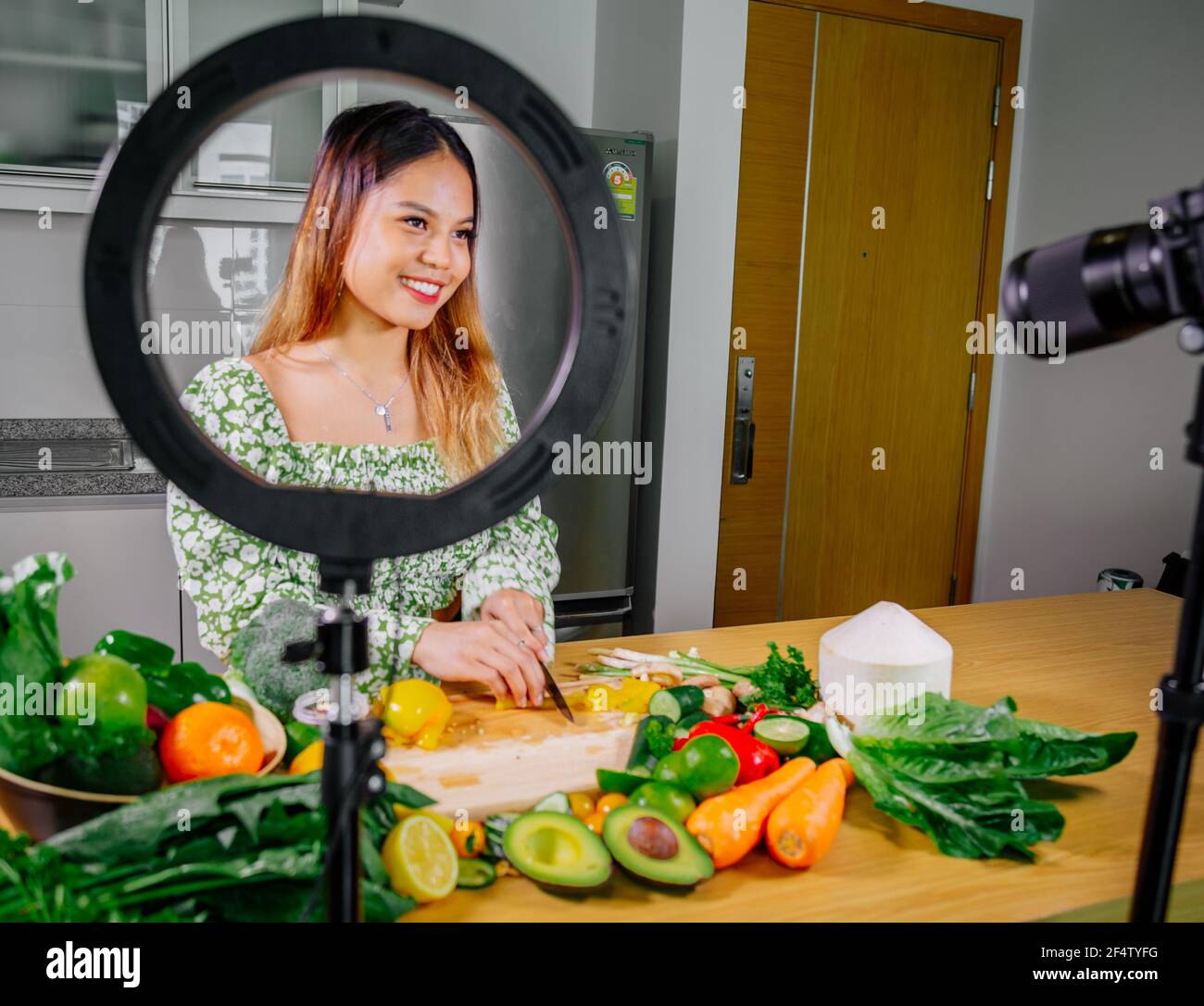 Asiatische Frau Blogger oder Content Creator Kochen und Aufnahme Videokamera. Zeigt gesunde Lebensmittel während der Aufnahme mit Kamera in der Küche. Stockfoto