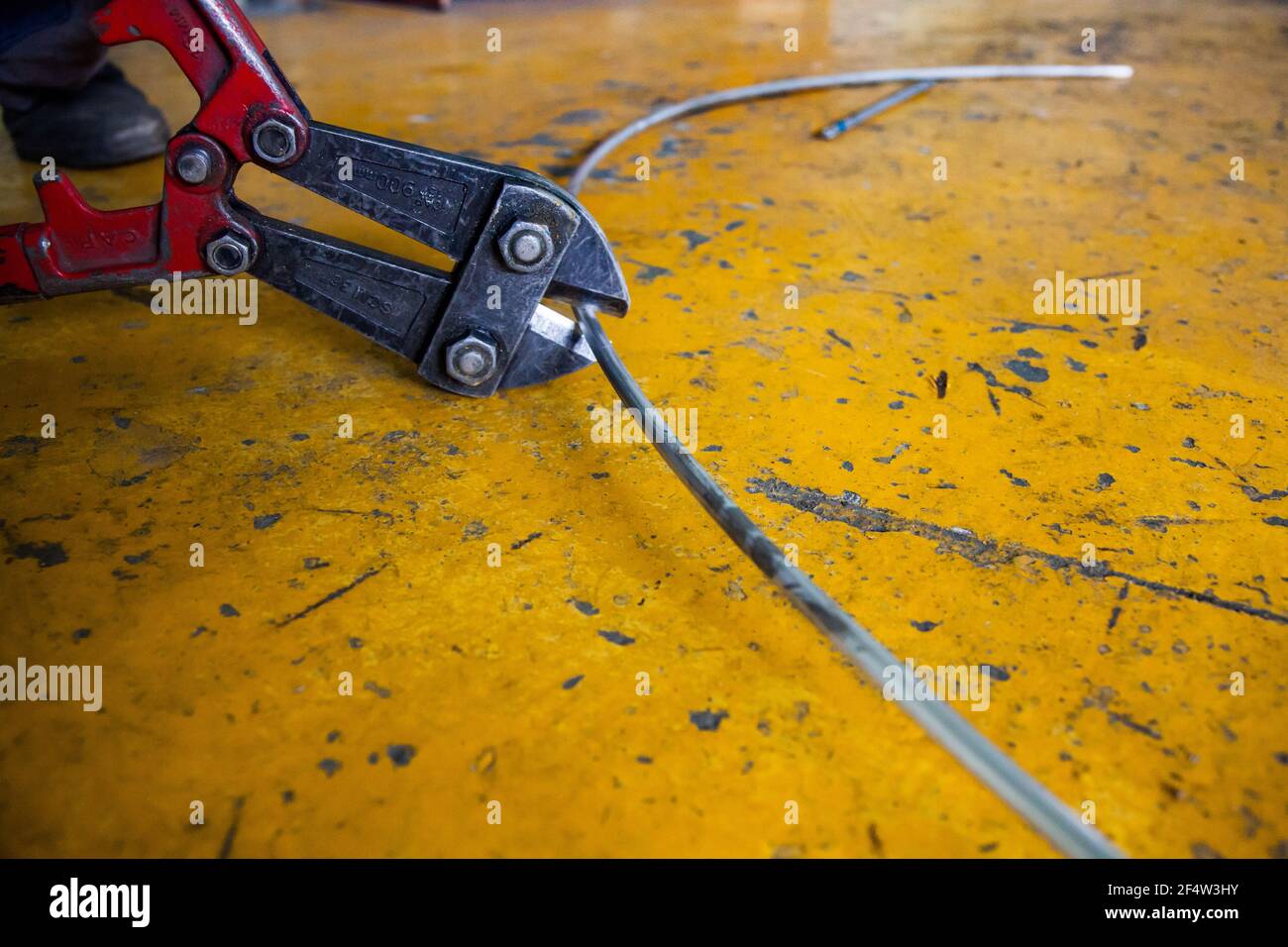 Große Schneidzange schneidet Aluminiumdraht. Gelber Beton gestrichenen Boden Hintergrund. Nahaufnahme. Stockfoto