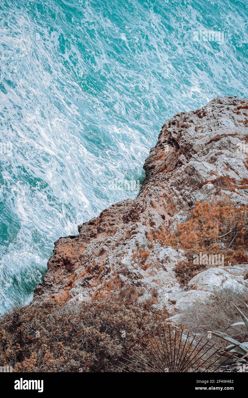 Wunderschöne Aussicht auf das wellige türkisfarbene Meer, das auf das Meer trifft Felsenklippe an der Küste Stockfoto