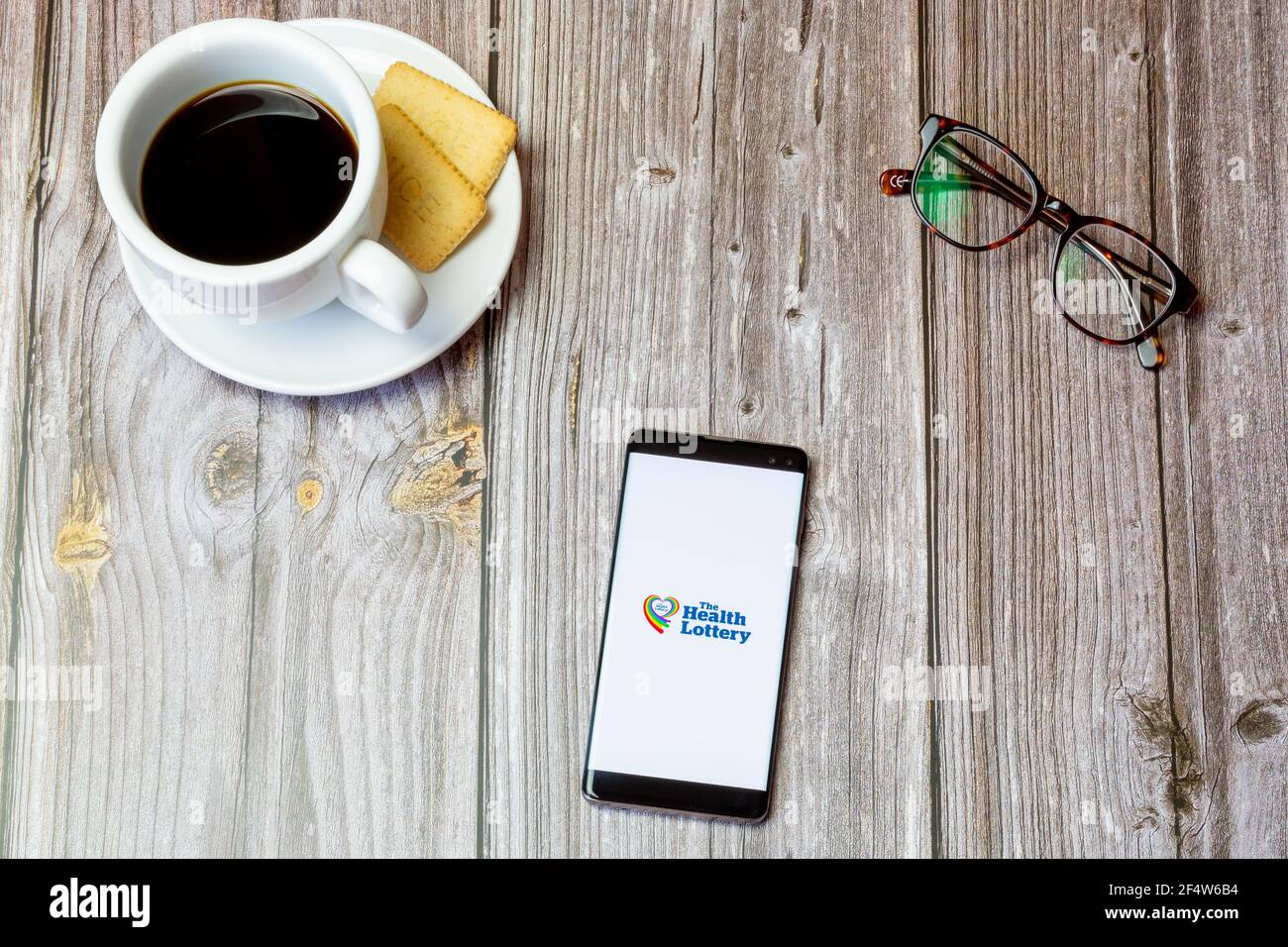Ein Handy oder Handy auf einem Holz gelegt Tabelle mit der Health Lottery App auf dem Bildschirm geöffnet Stockfoto