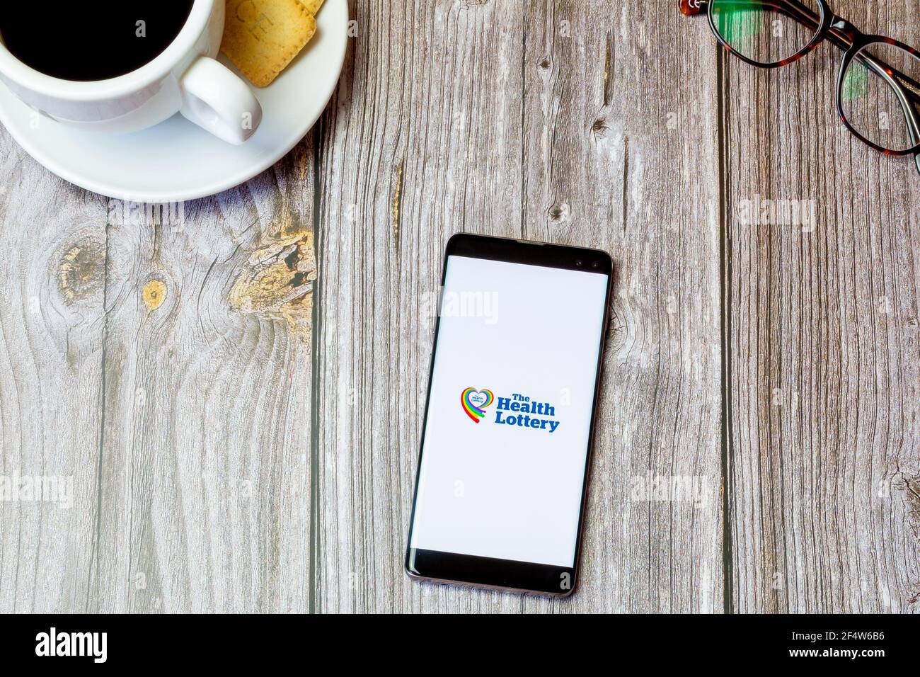 Ein Handy oder Handy auf einem Holz gelegt Tabelle mit der Health Lottery App auf dem Bildschirm geöffnet Stockfoto