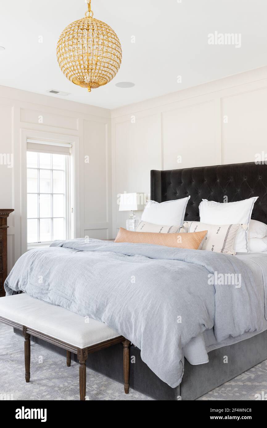 Ein schönes Schlafzimmer mit gemütlicher Bettwäsche unter einem luxuriösen, goldenen Kronleuchter mit Kristallen. Stockfoto