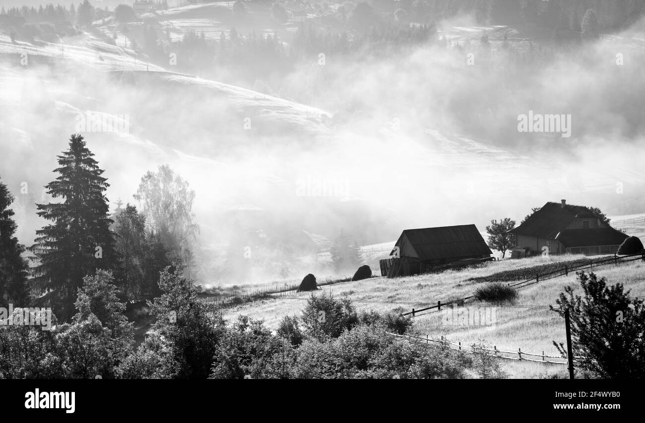 Bergwiese und alte Häuser im Nebel, abstrakter Hintergrund. Ukraine, Karpaten. Stockfoto