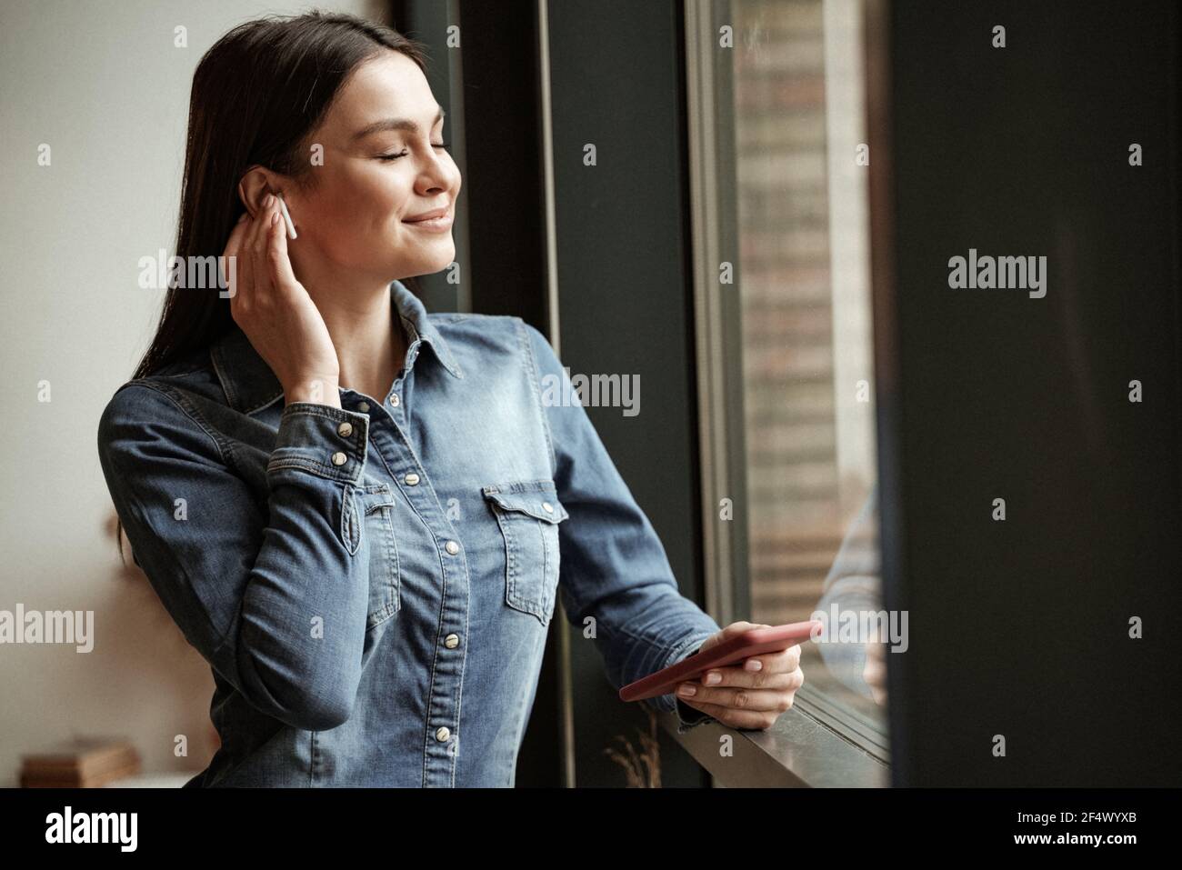 Zufrieden Frau in drahtlosen Ohrhörern Musik hören und halten Smartphone Stockfoto