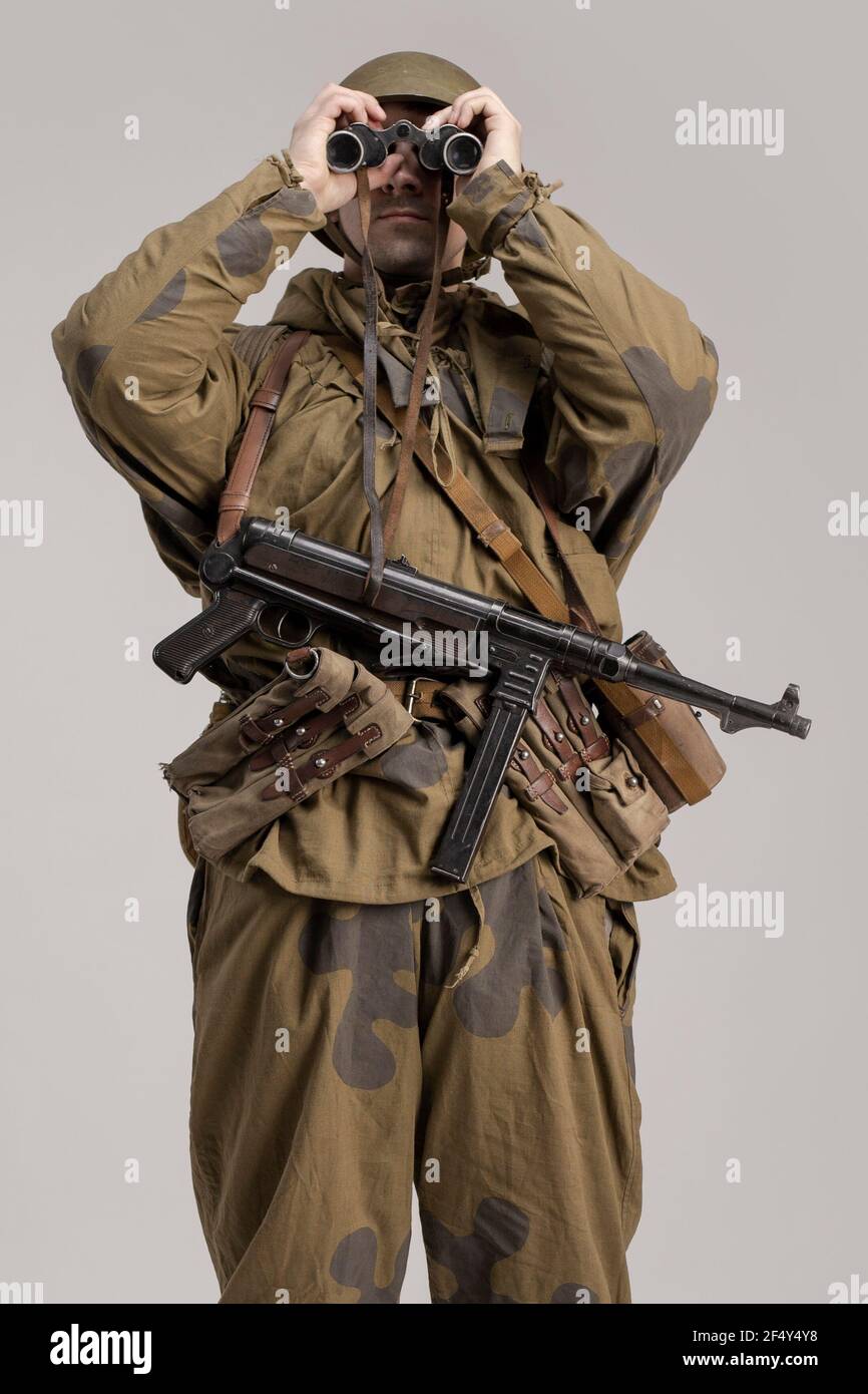 Erwachsener Mann mit Fernglas in der Hand in einer alten Militäruniform und Tarnkleidung eines Soldaten der sowjetischen Armee während des Zweiten Weltkriegs, 1943 Stockfoto