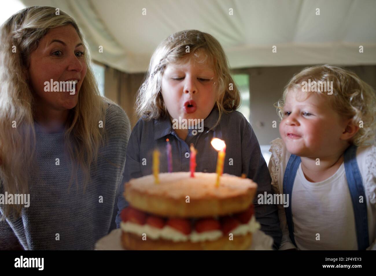 Happy boy bläst Geburtstagskerzen mit Familie Stockfoto