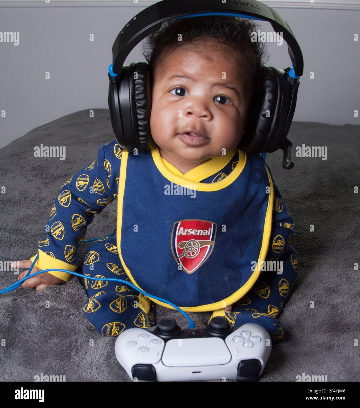 Niedlicher Junge in einem Arsenal Baby Grow posiert mit PS5 Kopfhörern Stockfoto