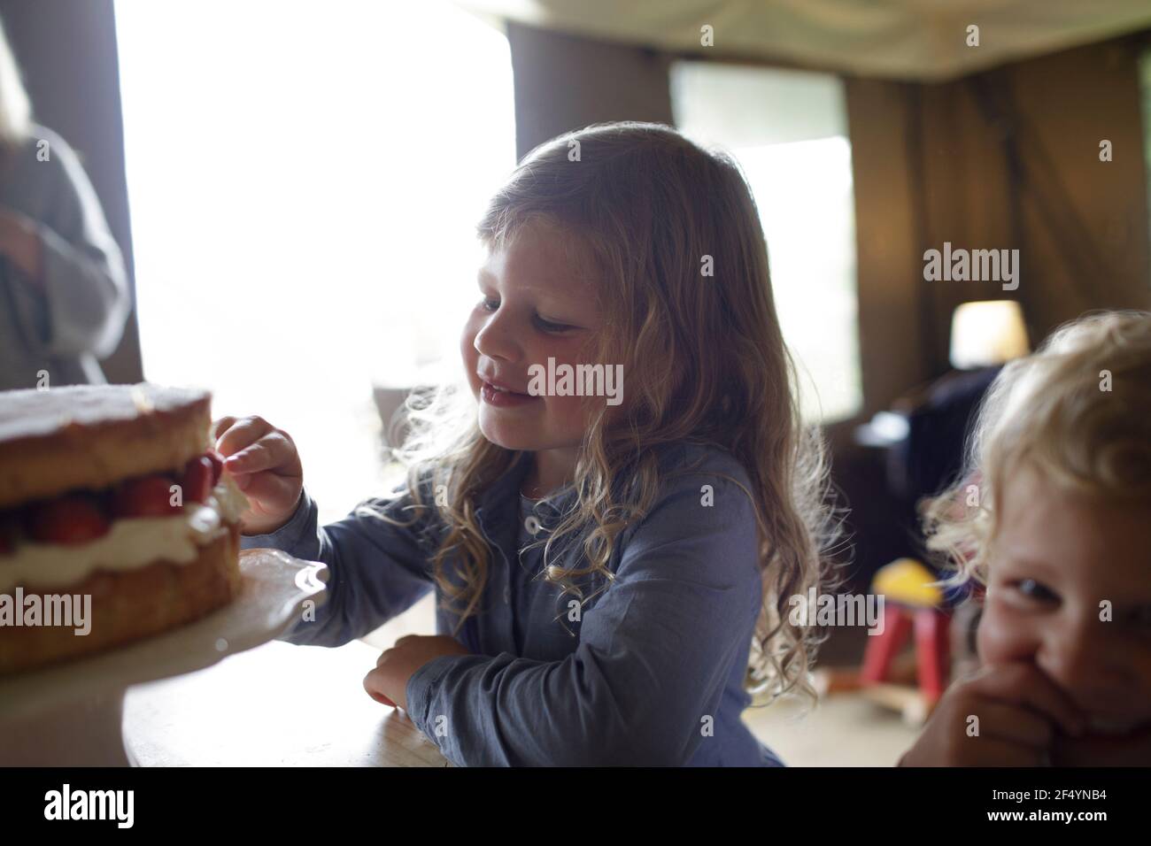 Nette Mädchen, die auf Erdbeerkuchen auf dem Tisch Stockfoto