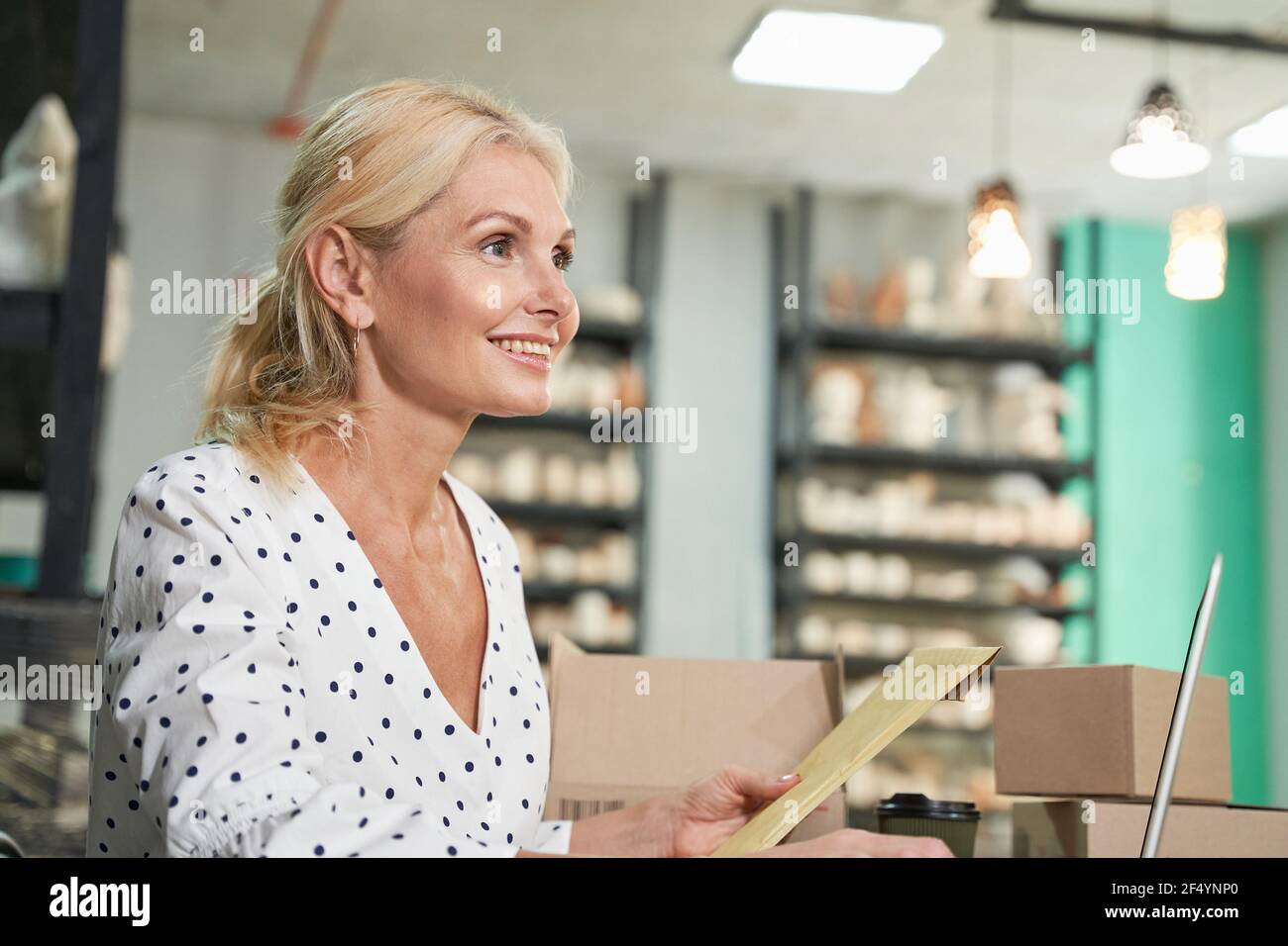 Nahaufnahme der erfolgreichen reifen Geschäftsfrau, Ladenbesitzer lächelnd, mit ihrem Laptop, empfangen Aufträge, während sie am Schreibtisch in ihrem Handwerk Keramik sitzen Stockfoto