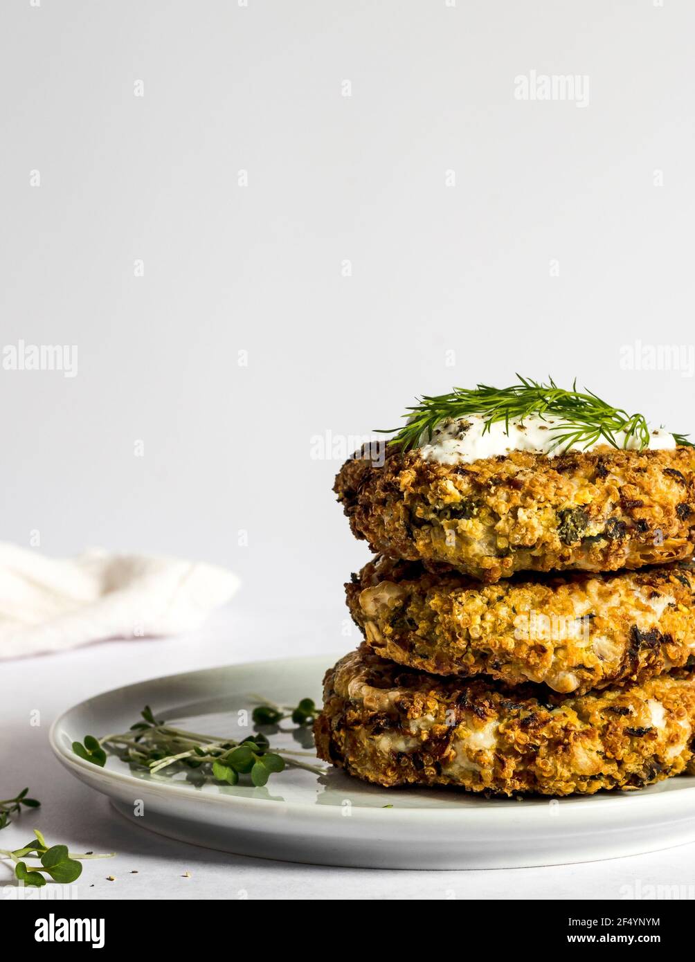 Dinner Scene - vegan gebackene Quinoa und Zucchini-Krapfen bereit zum Serentieren, mit frischem Dill, Mikrokräutern und veganer Sauerrahm. Stockfoto