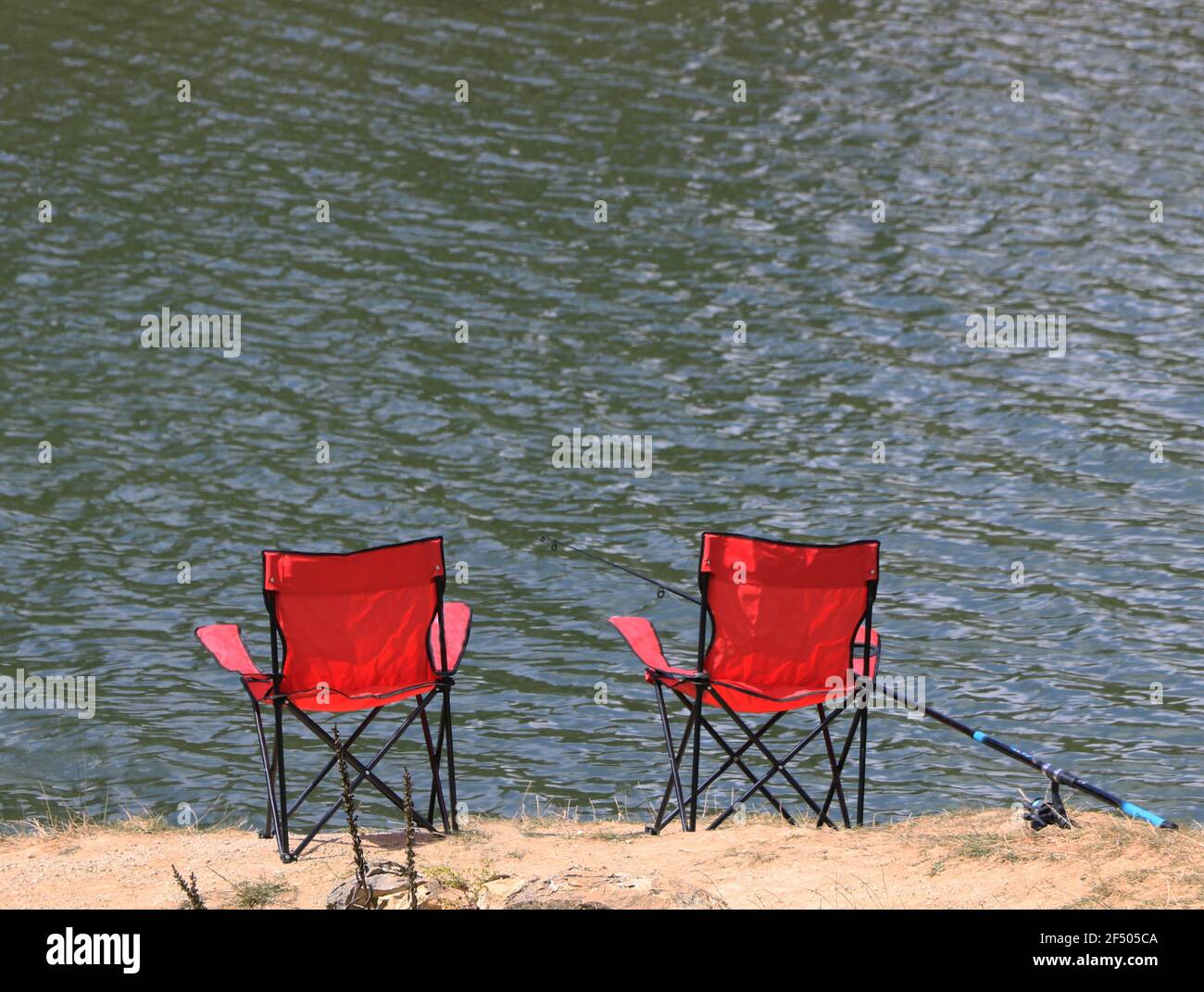 Klappbare rote Lagerstühle und Angelschnur in der Nähe des Sees Im Sommer Stockfoto