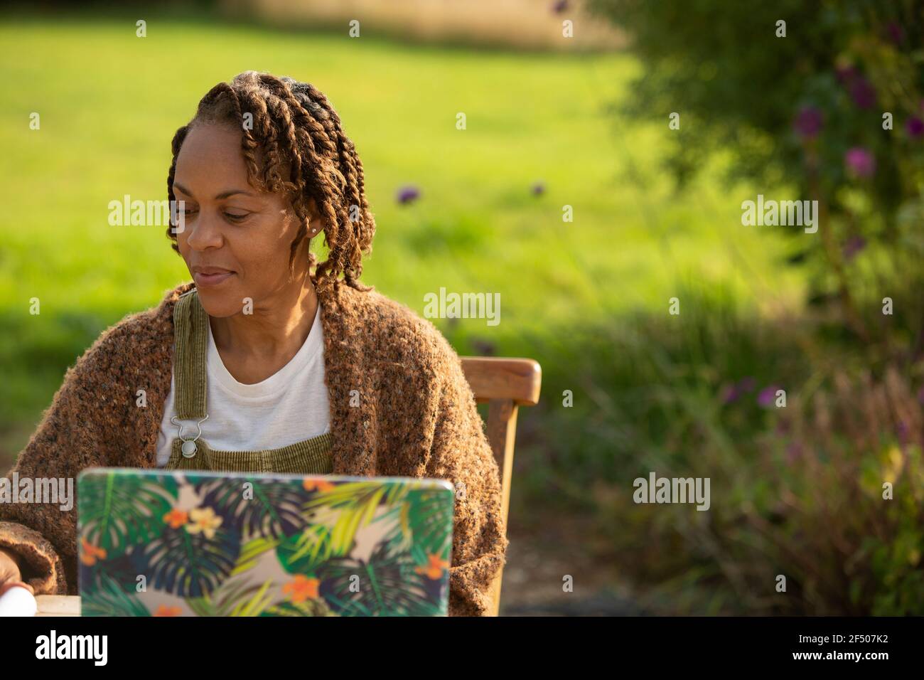 Frau, die am Laptop im sonnigen Garten arbeitet Stockfoto