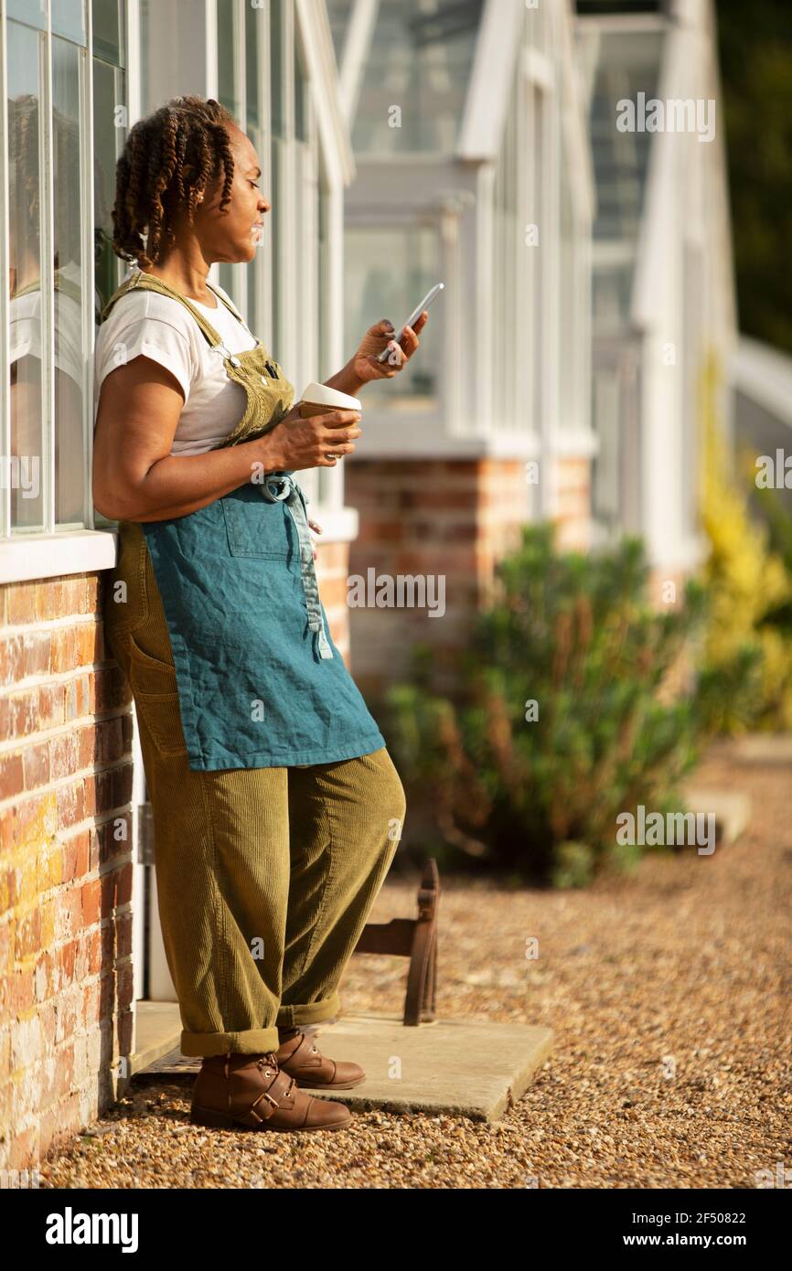 Weibliche Gartencenter Besitzer genießen Kaffeepause im sonnigen Gewächshaus Stockfoto