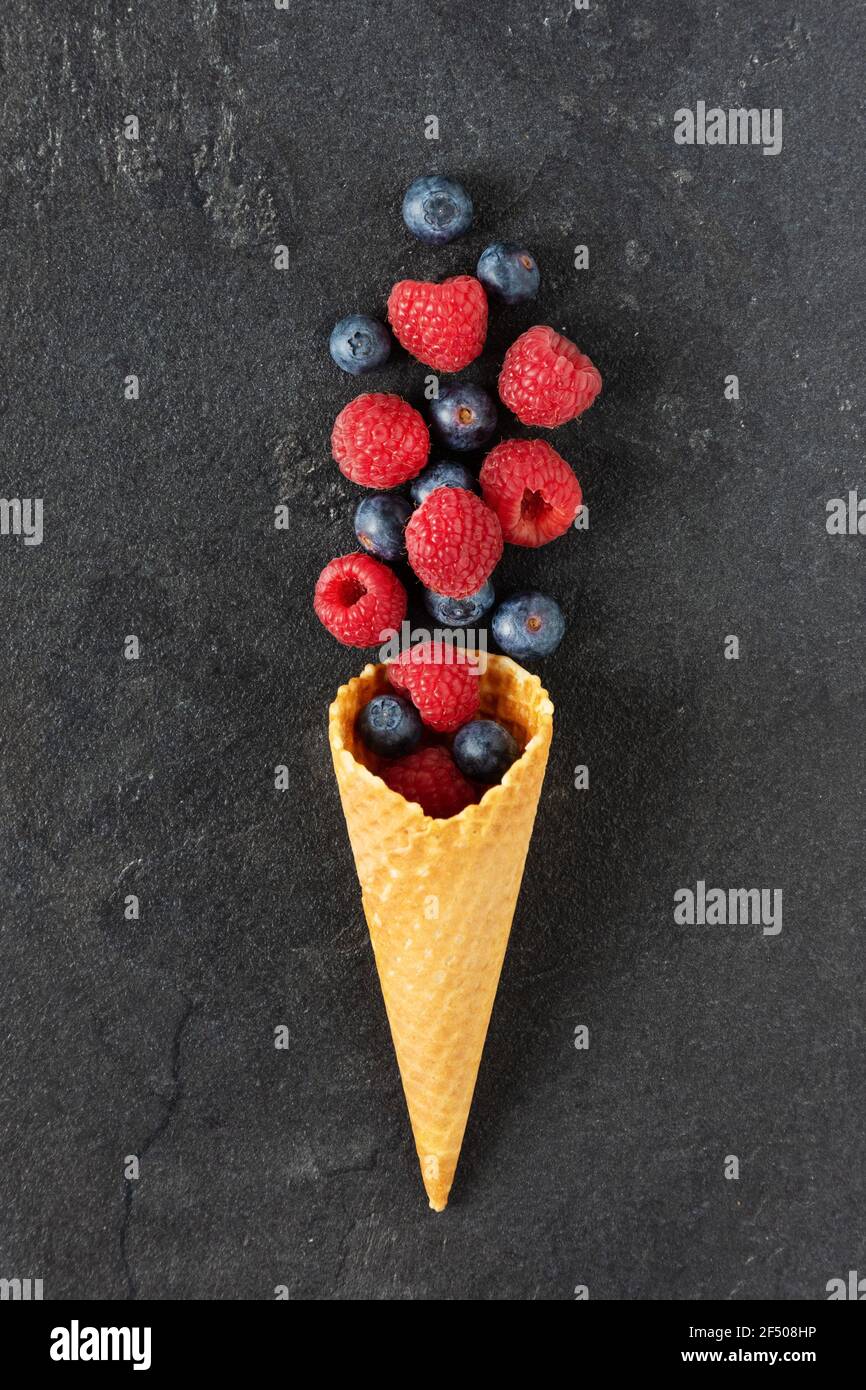 Mischung aus Heidelbeere und Himbeere in einem Waffel-Eis-Kegel auf schwarzem Hintergrund Draufsicht. Kreative Komposition mit wilden Sommerbeeren. Stockfoto