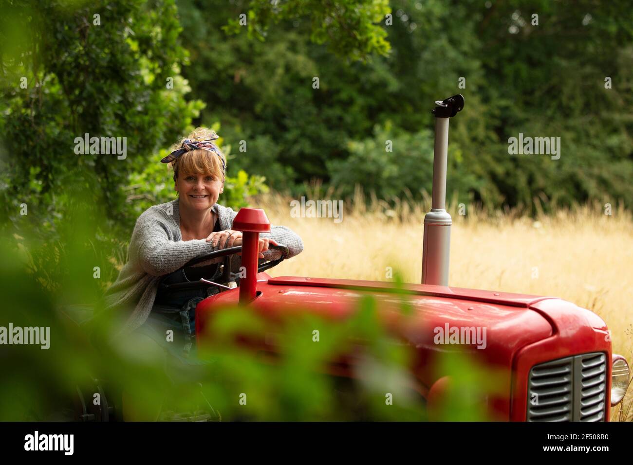Portrait glückliche Frau fahren Traktor in Obstgarten Stockfoto