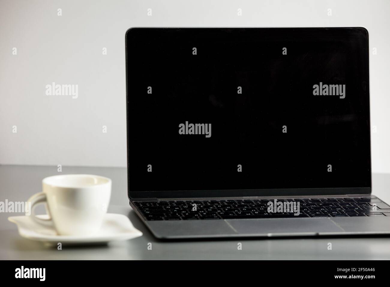 Modern geöffneter Laptop und Kaffeetasse auf Untertasse auf dem grauen Tisch auf weißem Hintergrund. Remote-Job, Home Office. Moke up mit Laptop und Kaffeetasse. Stockfoto