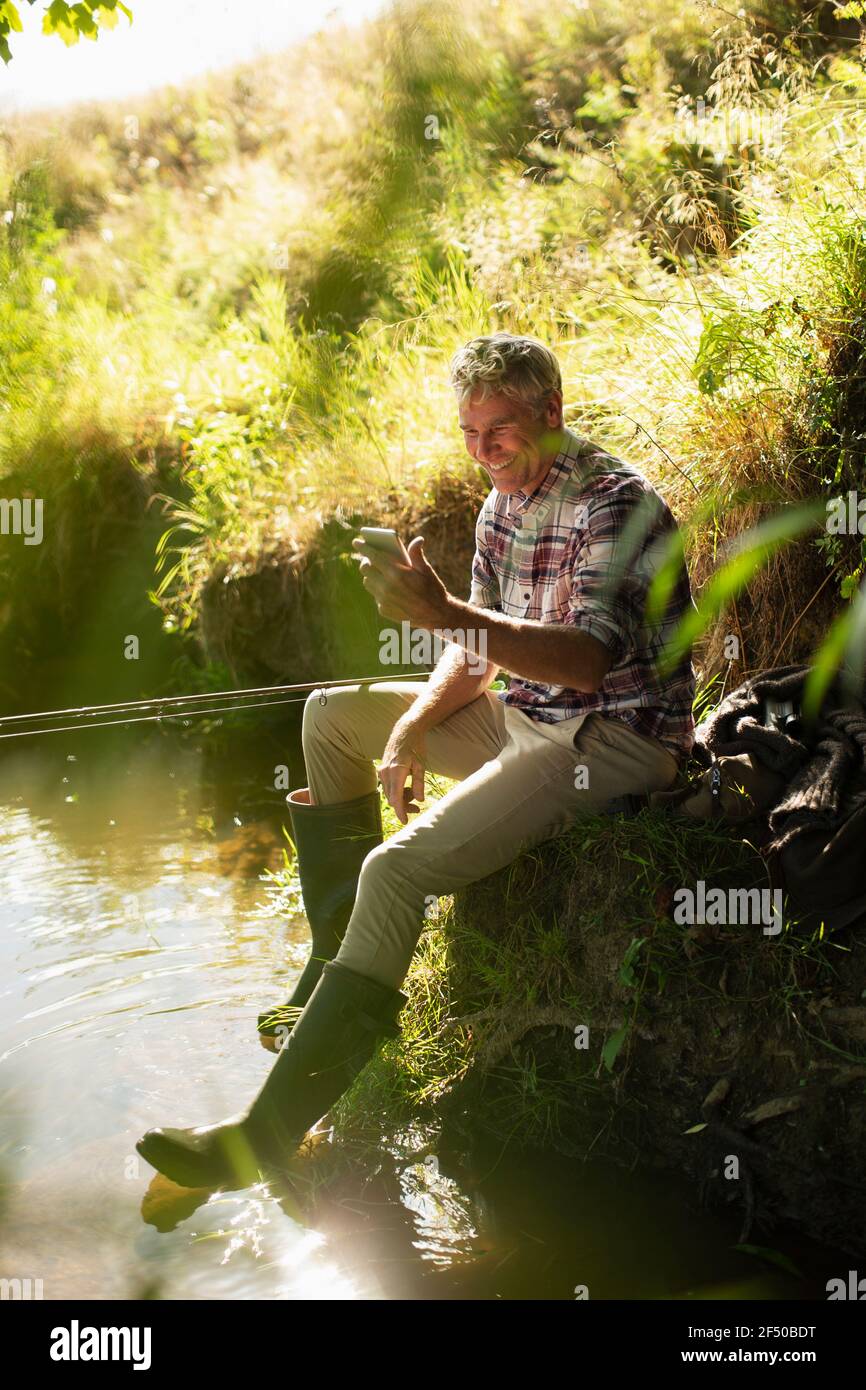 Mann Fliegenfischen und mit Smartphone am sonnigen Flussufer Stockfoto