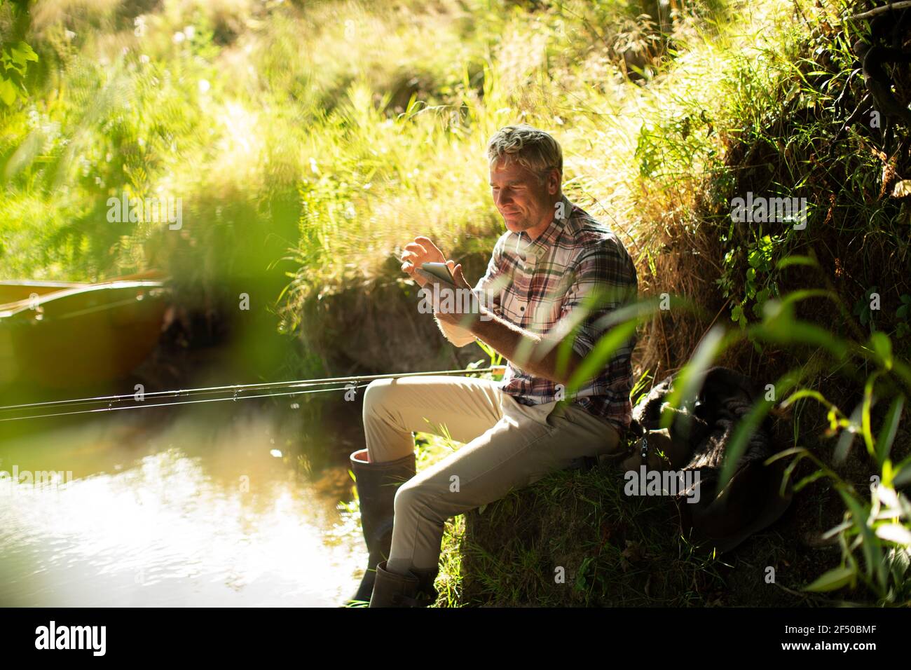 Mann Fliegenfischen und mit Smartphone am sonnigen Flussufer Stockfoto