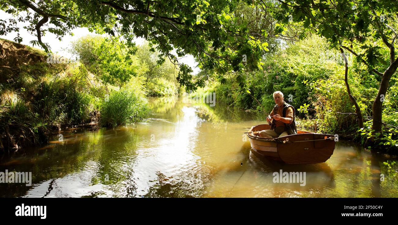 Mann Fliegenfischen vom Boot auf ruhigen grünen Fluss Stockfoto