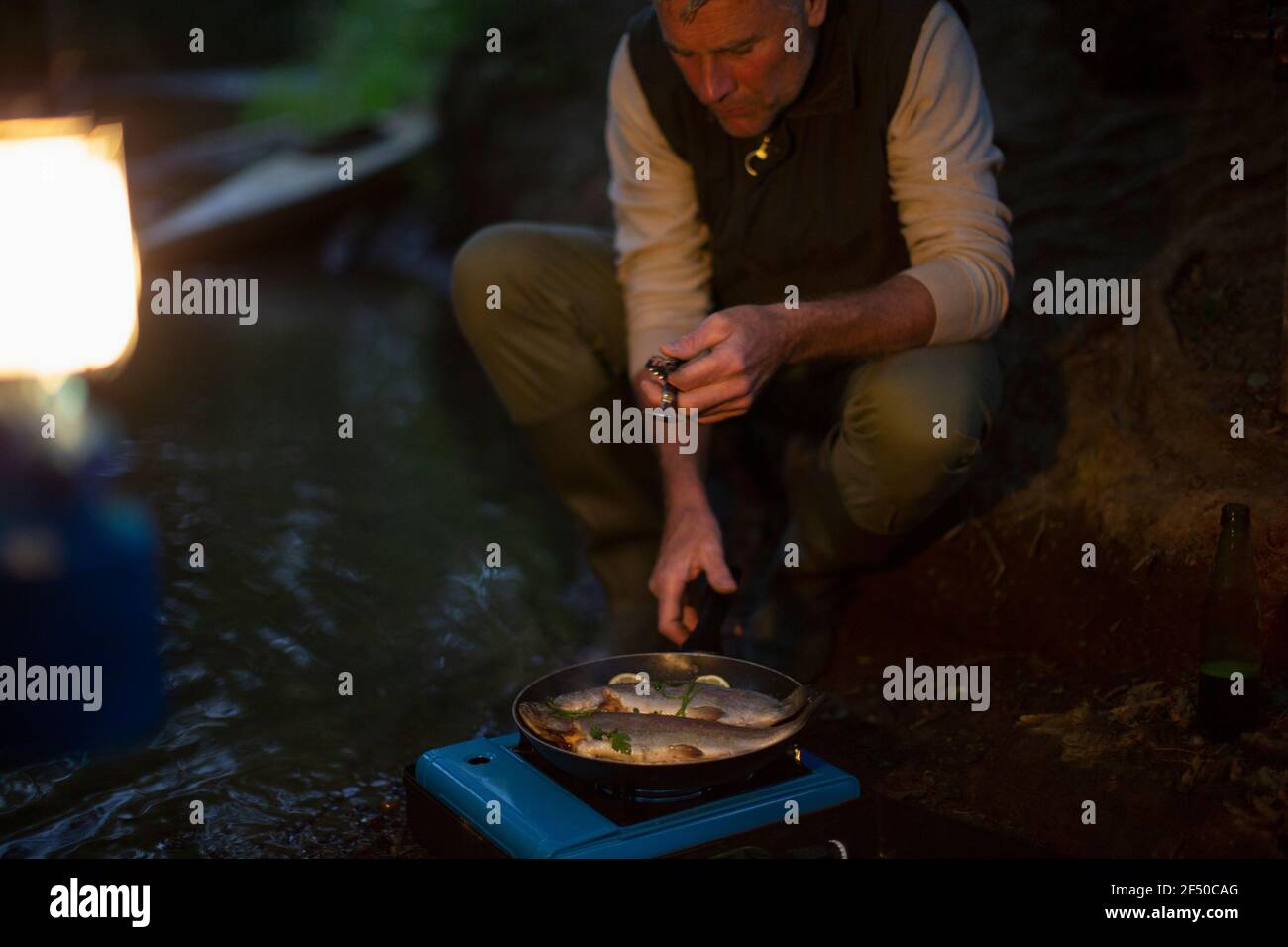 Mann kocht frisch gefangenen Fisch auf Campingkocher in der Nacht Stockfoto