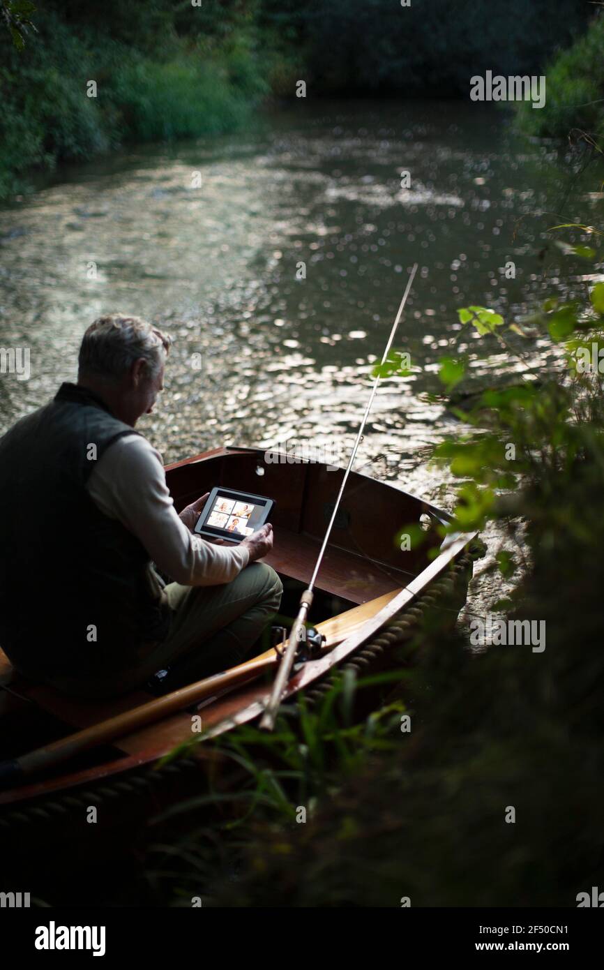 Mann Fliegenfischen und Video-Chat mit digitalen Tablet in Boot Stockfoto