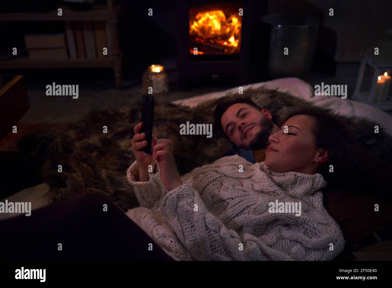 Zärtliches Paar mit Smartphone auf Decken am gemütlichen Kamin Stockfoto